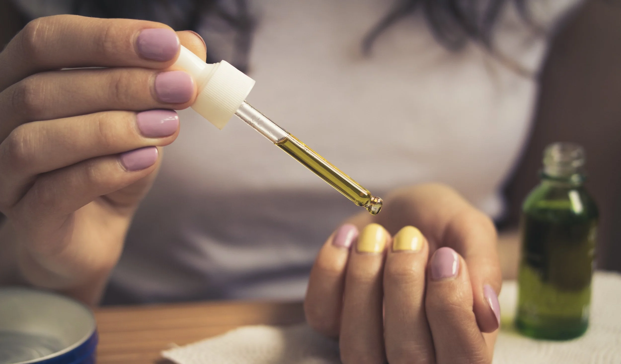 Female hands take care of cuticles with oil. Girl in white t-shirt sitting at the table and takes care of her cuticles. She has a bright manicure. On the table lay manicure equipment. Vintage filter
