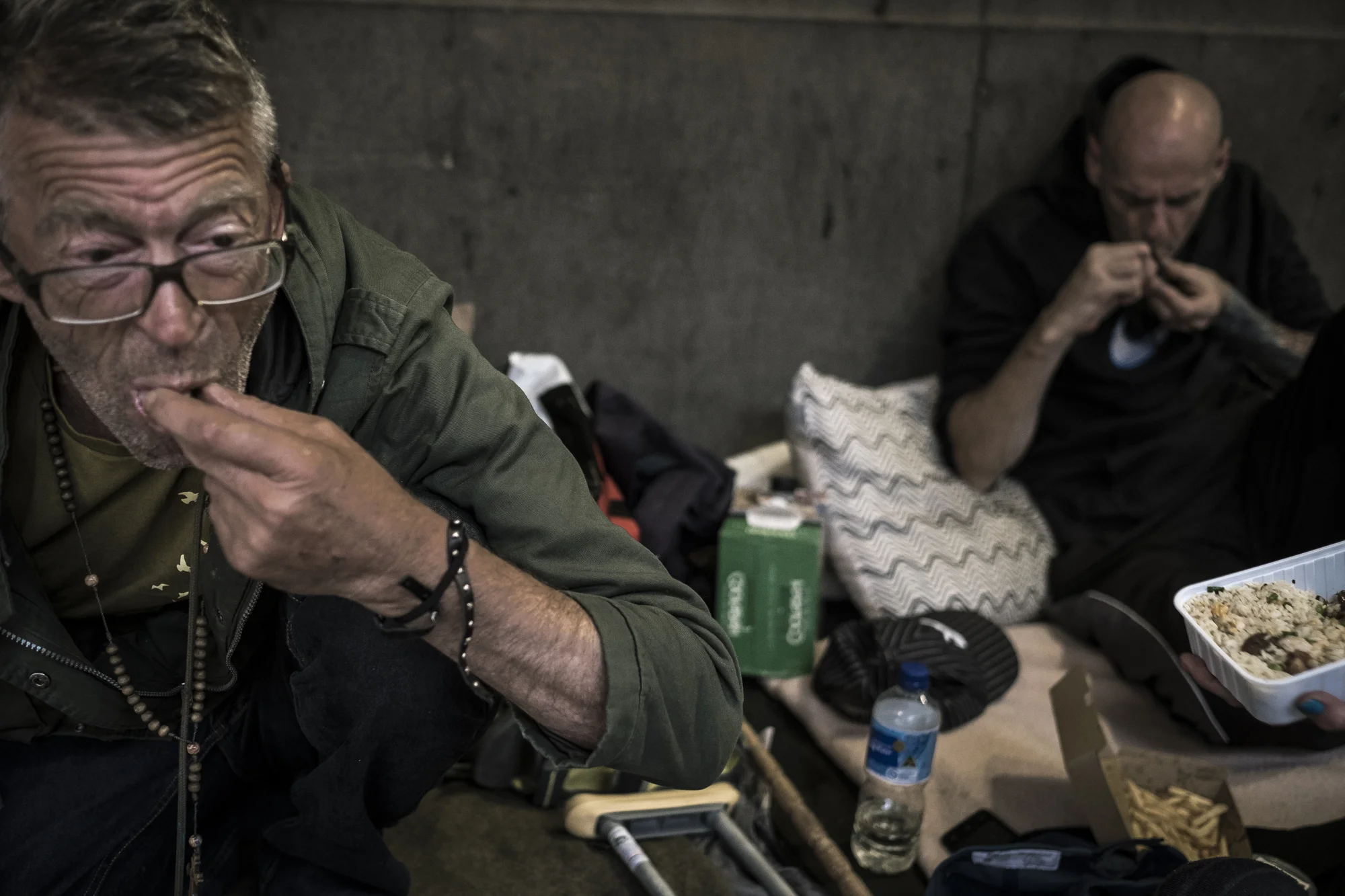  Flinders Street, Melbourne, Australia. Asha Lang sits eating a meal given to him by a member of the public while another homeless man and Asha's &nbsp;'neighbour' smokes ice through a crack-pipe behind him in full public view on the streets of Melbo