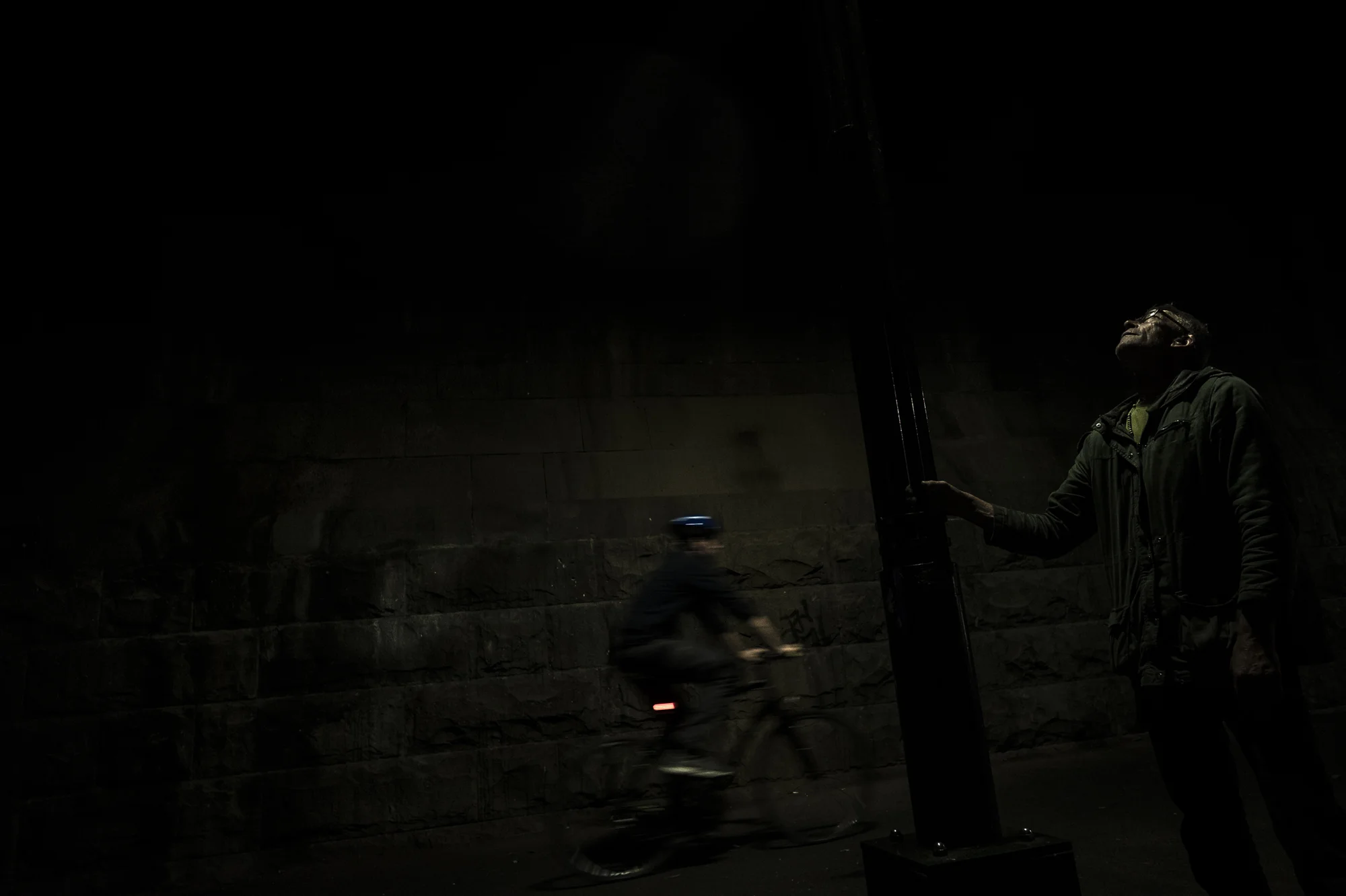  Southbank, Melbourne, Australia. Asha Lang is seen staring at a street lamp as cyclists ride by in an underpass. &nbsp;“A friend of my fathers stood above me and asked what I wanted to do when I grew up. I looked up at him, saw the light of his ciga