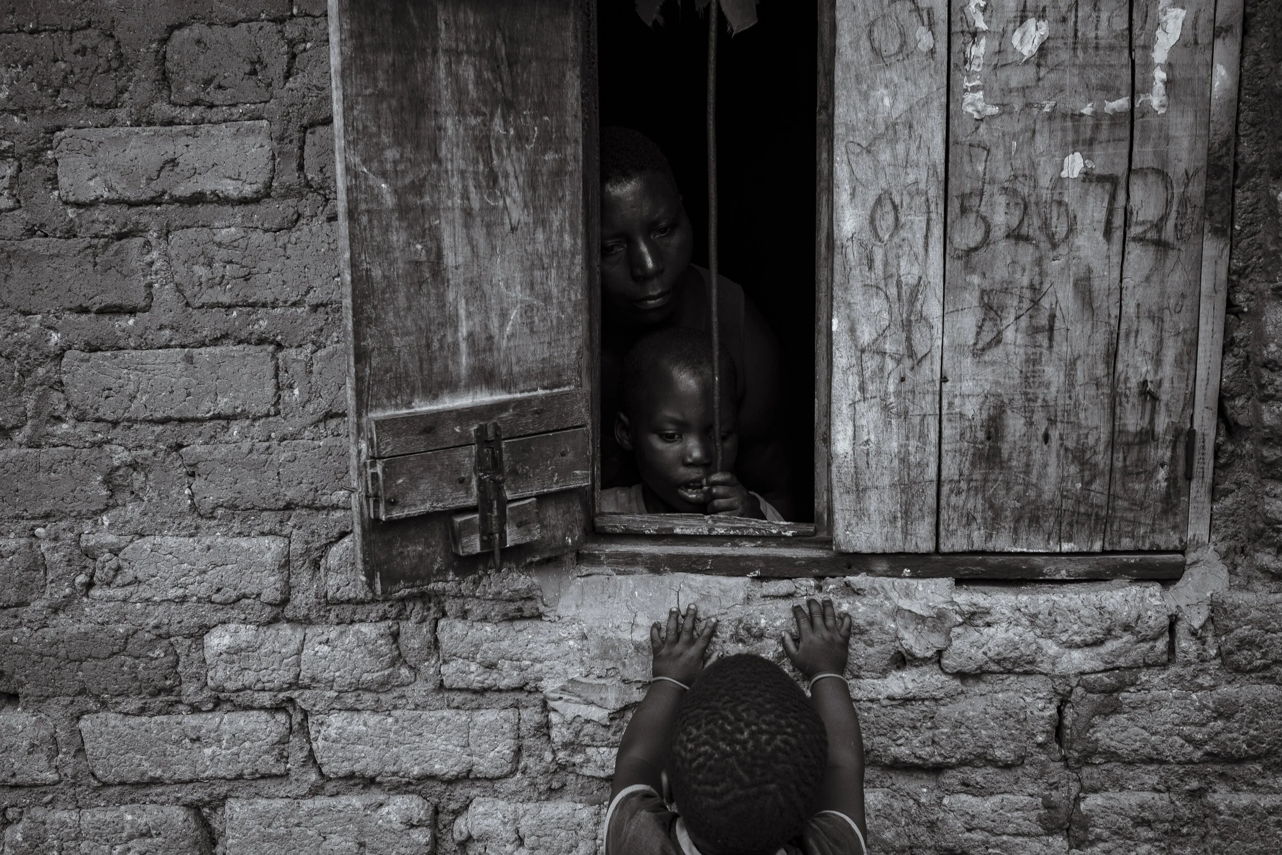  Lugonjo, Uganda. Nono Zubeda and her daughter, Salma Kobusinge peer outside their home as a local neighbours child looks in. Nono has spent time in prison for leaving Salma unattended in the dilapidated two room house in a suburb of Entebbe. Salma's