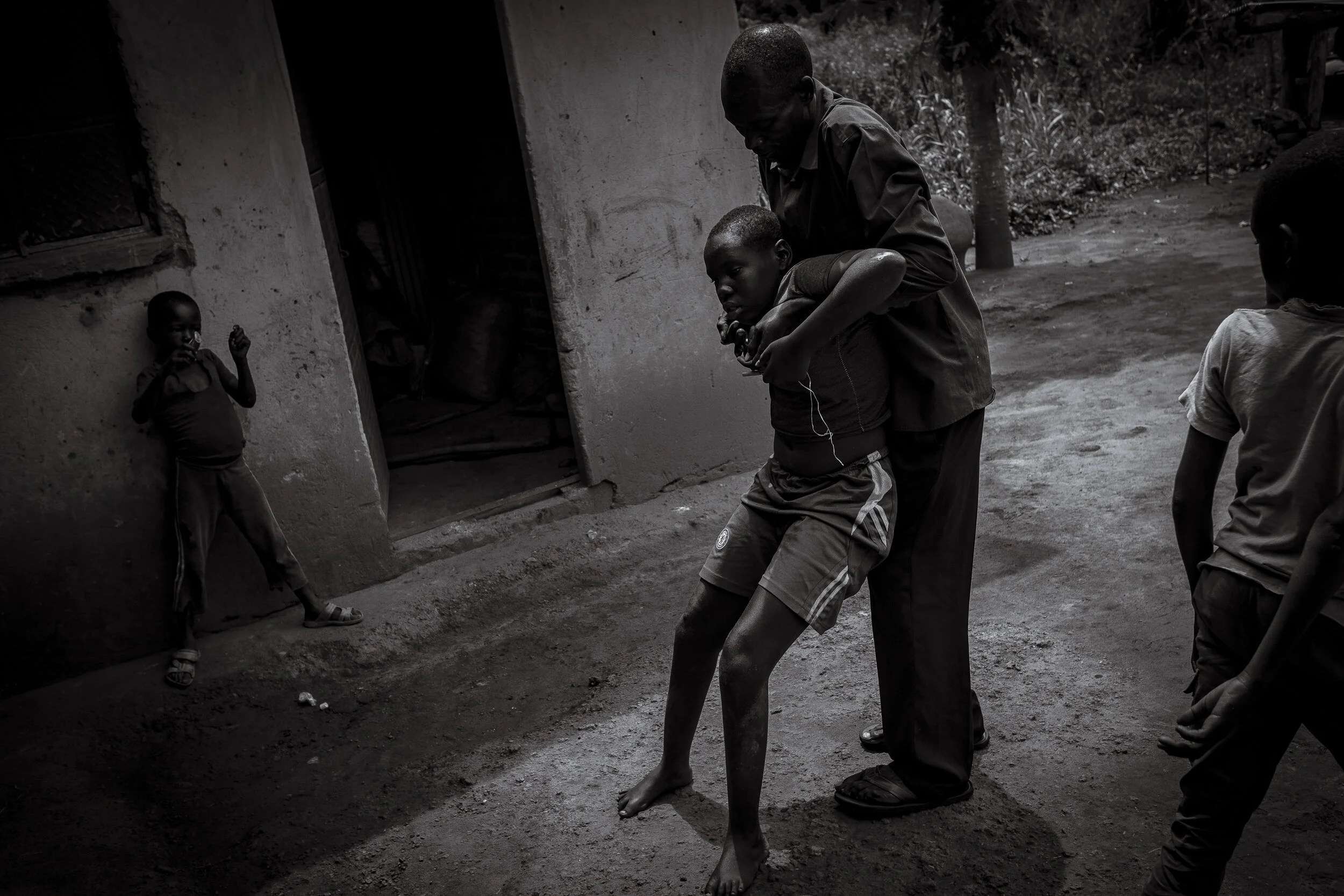  Anai Agali, Lira District. George Abaa carries his his eleven year old daughter Naomi Ecuto into the shade where she can sit in an upright position. Community health outreach workers have told George that due to her spine curvature, it is better for