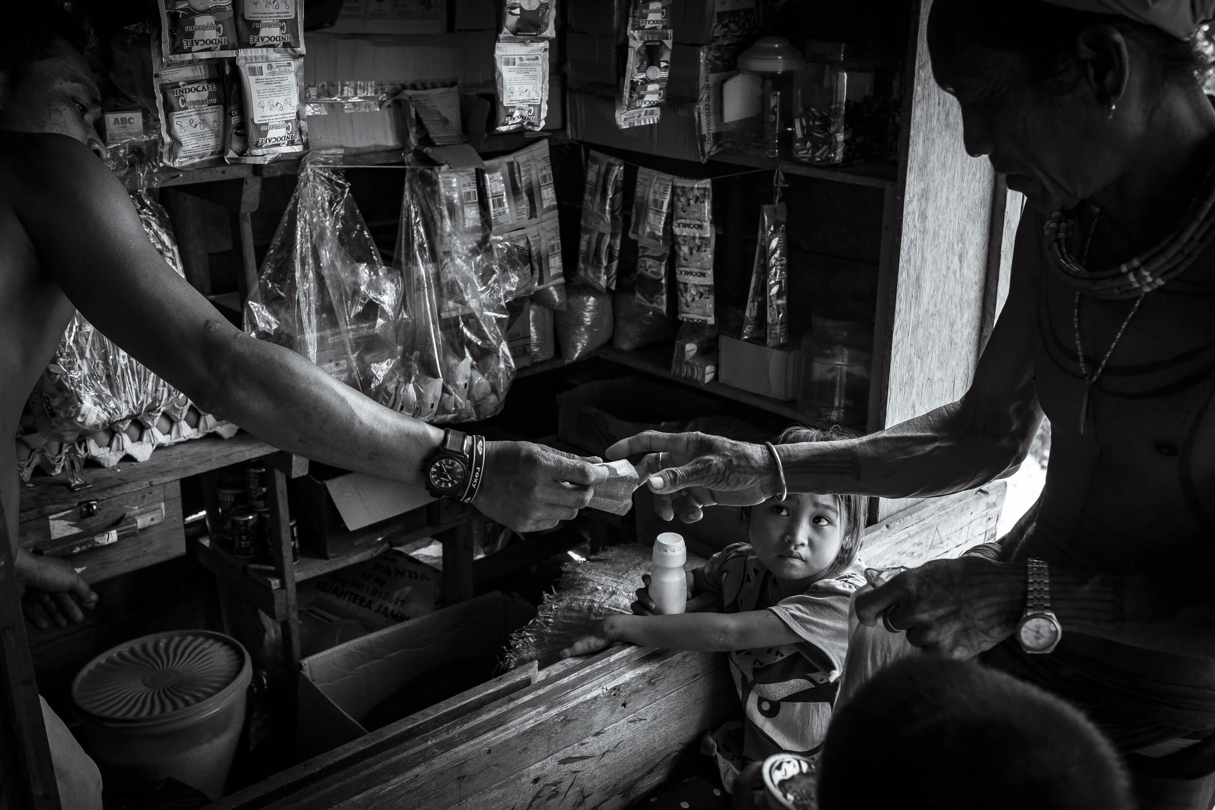  Ukan watches on as Masit Dere pays for a treat in the small shop in Matatonan. Further adding to the worrying trend towards modern societal systems, the small shop only sells products that are high in sugar and additives that the Mentawai have not y