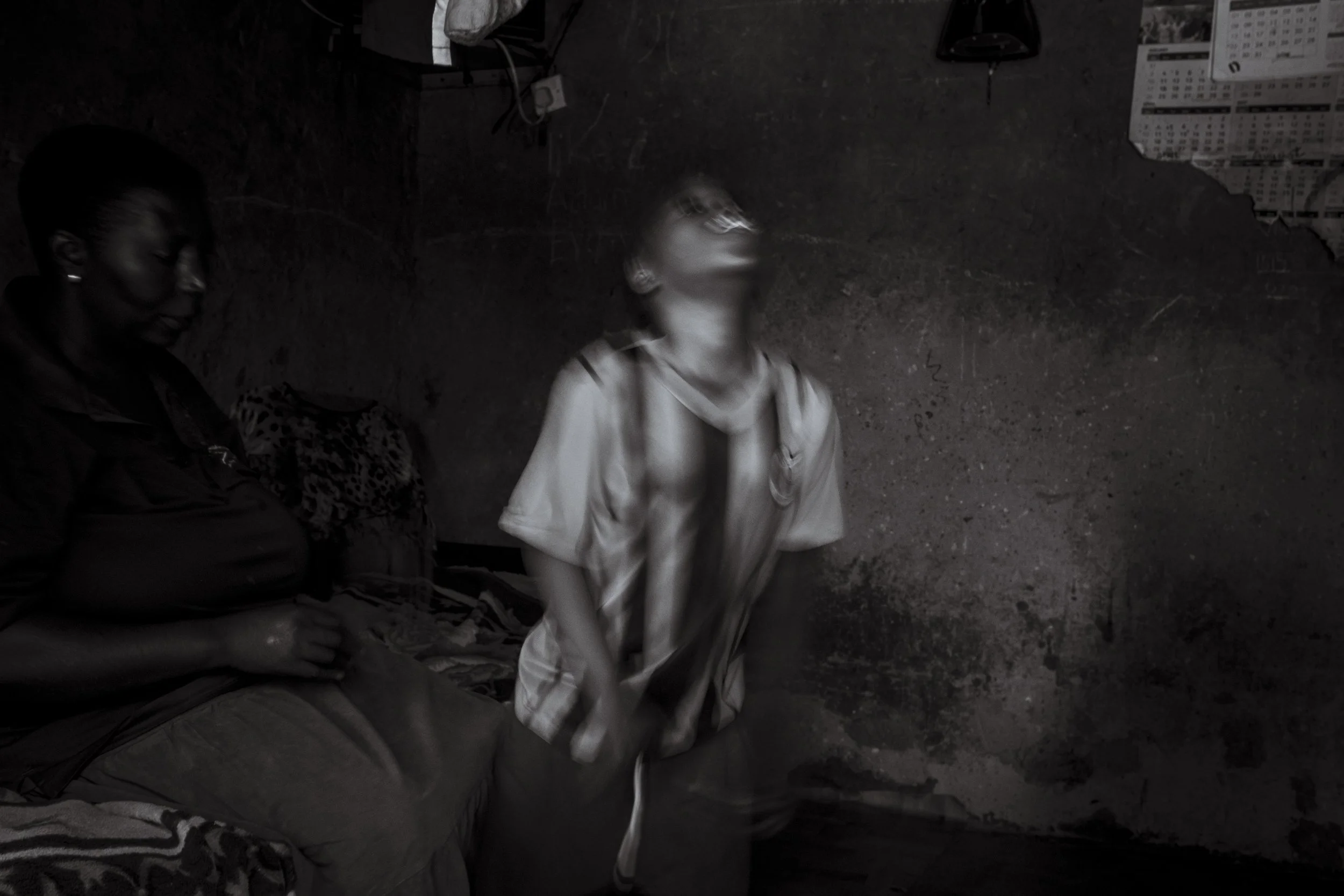  17 July 2023. Lugonjo, Uganda. Single mother Nono Kabenge watches on as  her 11-year-old daughter Salma stumbles towards the light of an open doorway.   Salma lives with epilepsy, Sickle Cells, Autism and is non verbal, partially blind and deaf. Sal