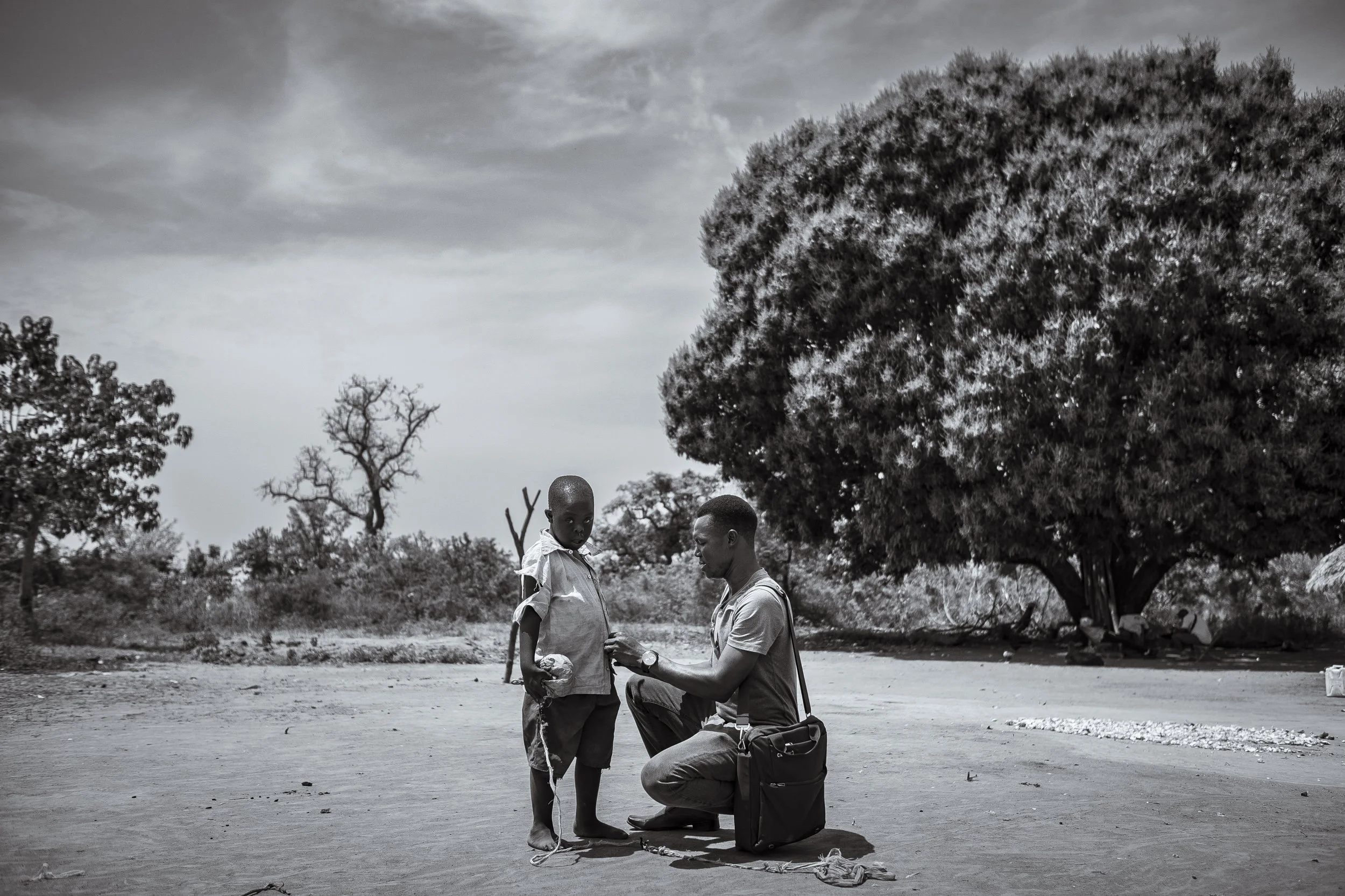  27 February 2020. Obur, Soroti District, Uganda. Outreach worker Pastor Fred Alimet buttons up  thirteen-year-old Silus Odii's shirt after releasing him from his restraint.   Silus, who lives with Down Syndrome, regularly gets tethered to a wooden c