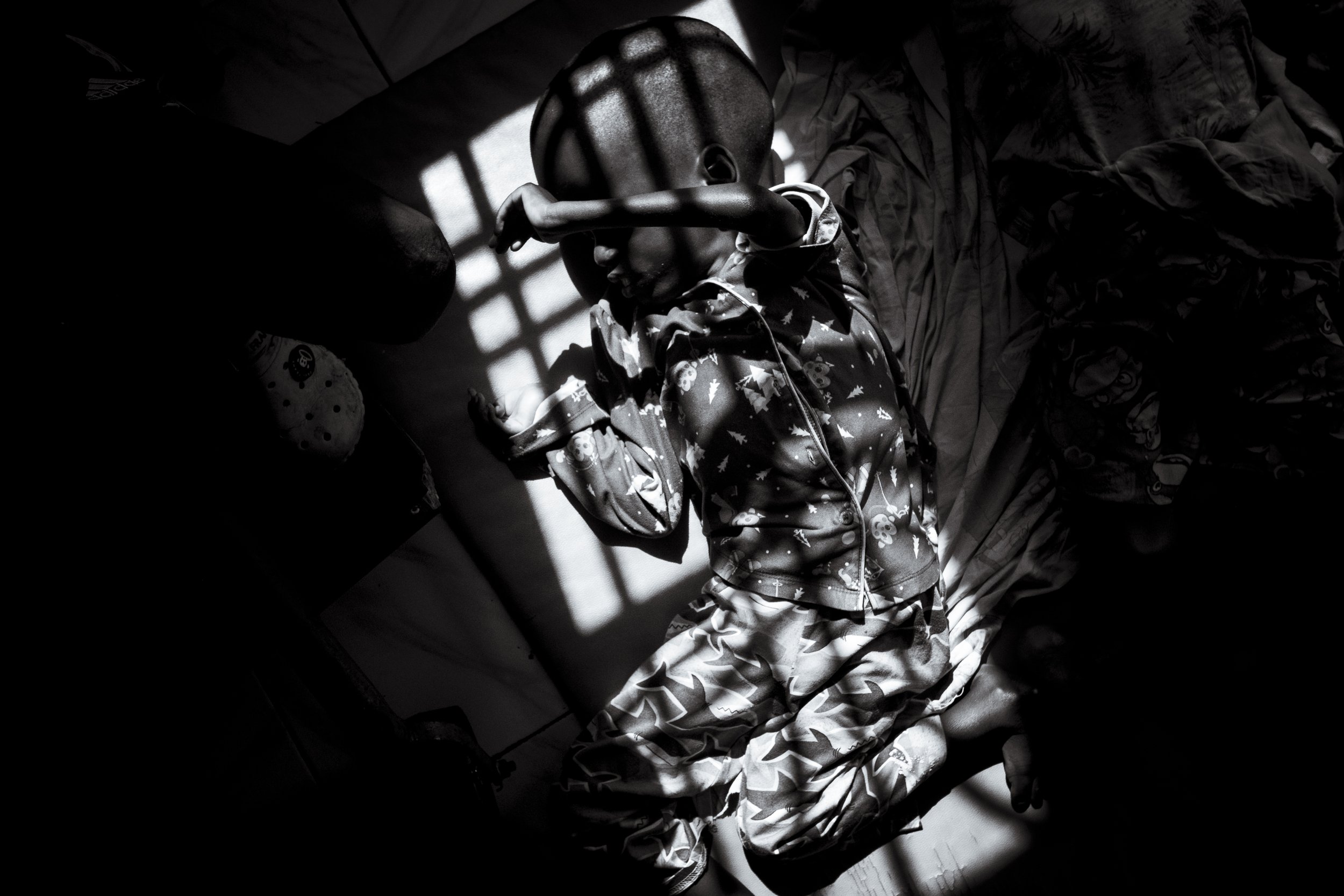  25 July 2023. Bugembe, Jinja District, Uganda. A young boy with Hydrocephalus is seen illuminated by window light on the floor at Hope of Hope, Jinja, Uganda.   The Home of Hope houses over 90 children who have been abandoned due to their intellectu