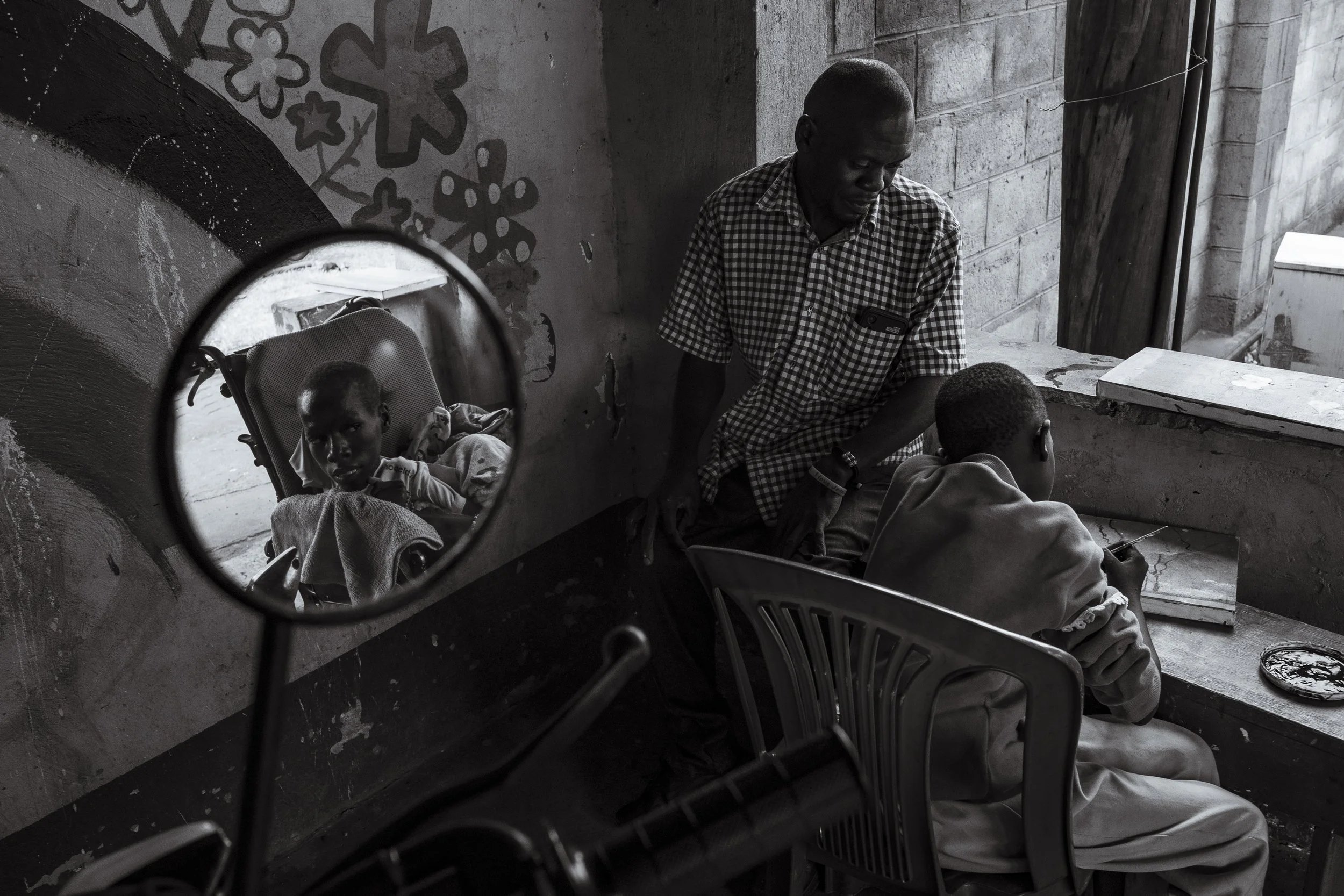  27 November 2024. Bugembe, Jinja District, Uganda. Daniel, 18, looks on as Mary works on a painting in a weekly skilling program held at Home of Hope. The skilling program is run three times a week where the children learn various forms of art and c