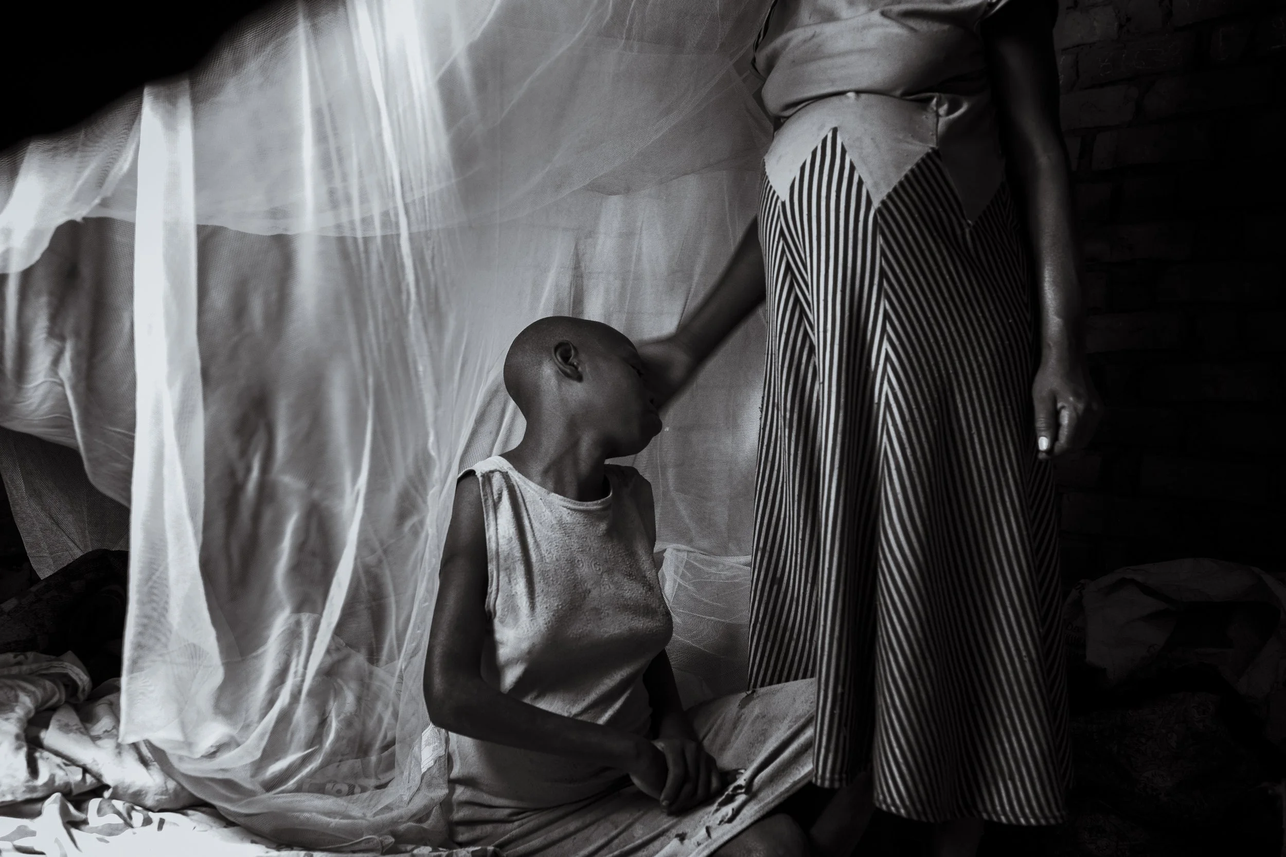  28 November 2024. Busede, Uganda. 13-year-old Janet Akwatulira is comforted by her mother Florence Nakecho in the bedroom they share with Janet's sister Jimbo. Janet and Jimbo both live with undiagnosed intellectual disabilities. Janet is currently 