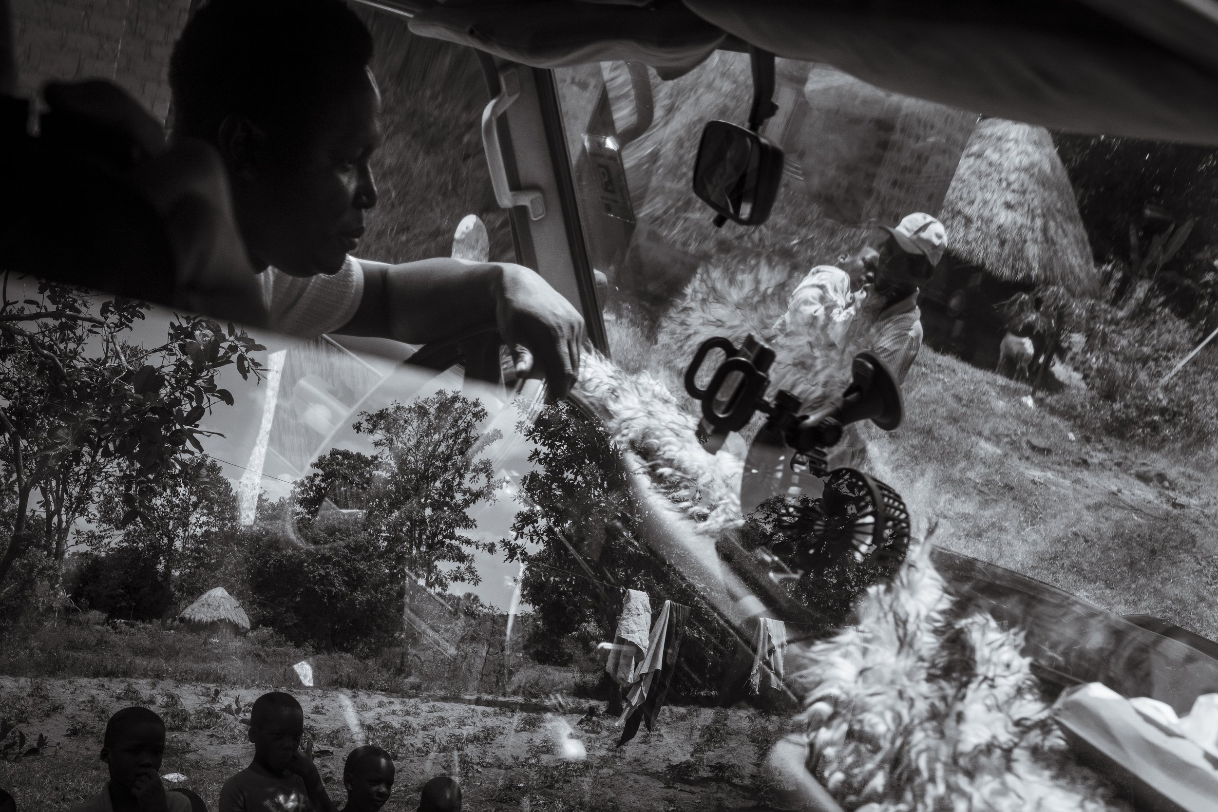  2 December 2024. Oukot, Amuria District, Soroti. Local children watch on as Simon Okurut carries his son Paul Oribo, who lves with Cerebral Palsy, to the Landcruiser Fred Alimet from local charity Cherish Ikoku Uganda uses as a makeshift ambulance. 