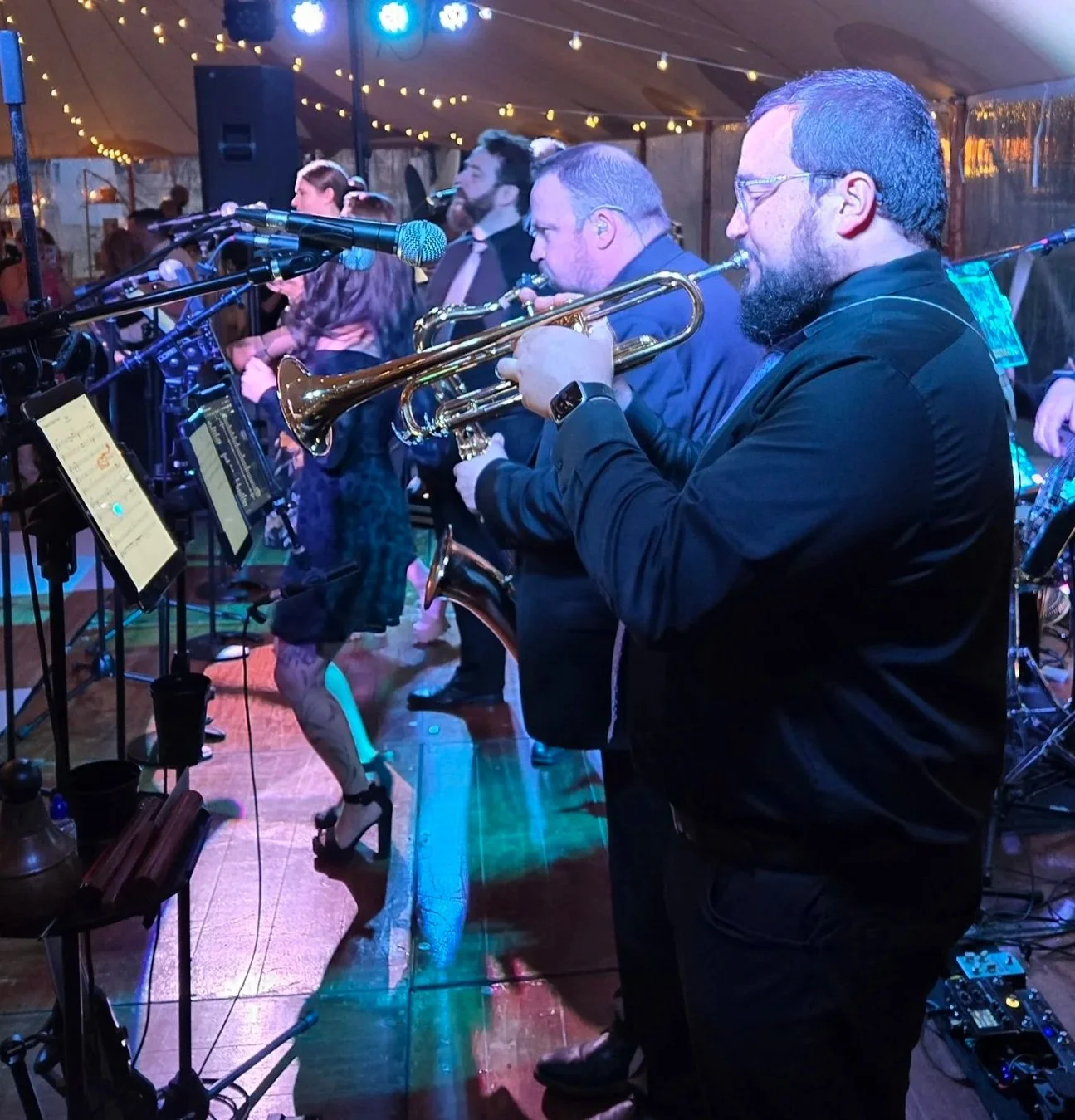 Musicians playing brass instruments at a lively indoor event with colorful hanging lights.