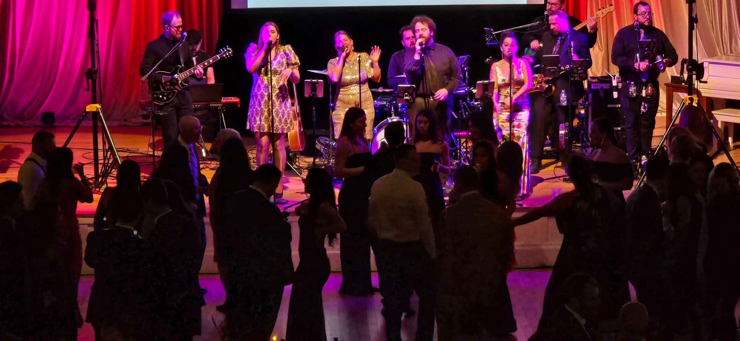 Musicians performing on stage with a band at a lively event, audience dancing in front of the stage.