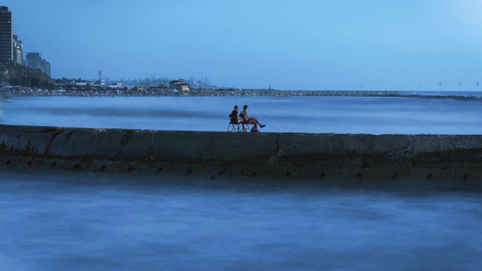 צילום אומנותי של זוג שיושב על גשר בים