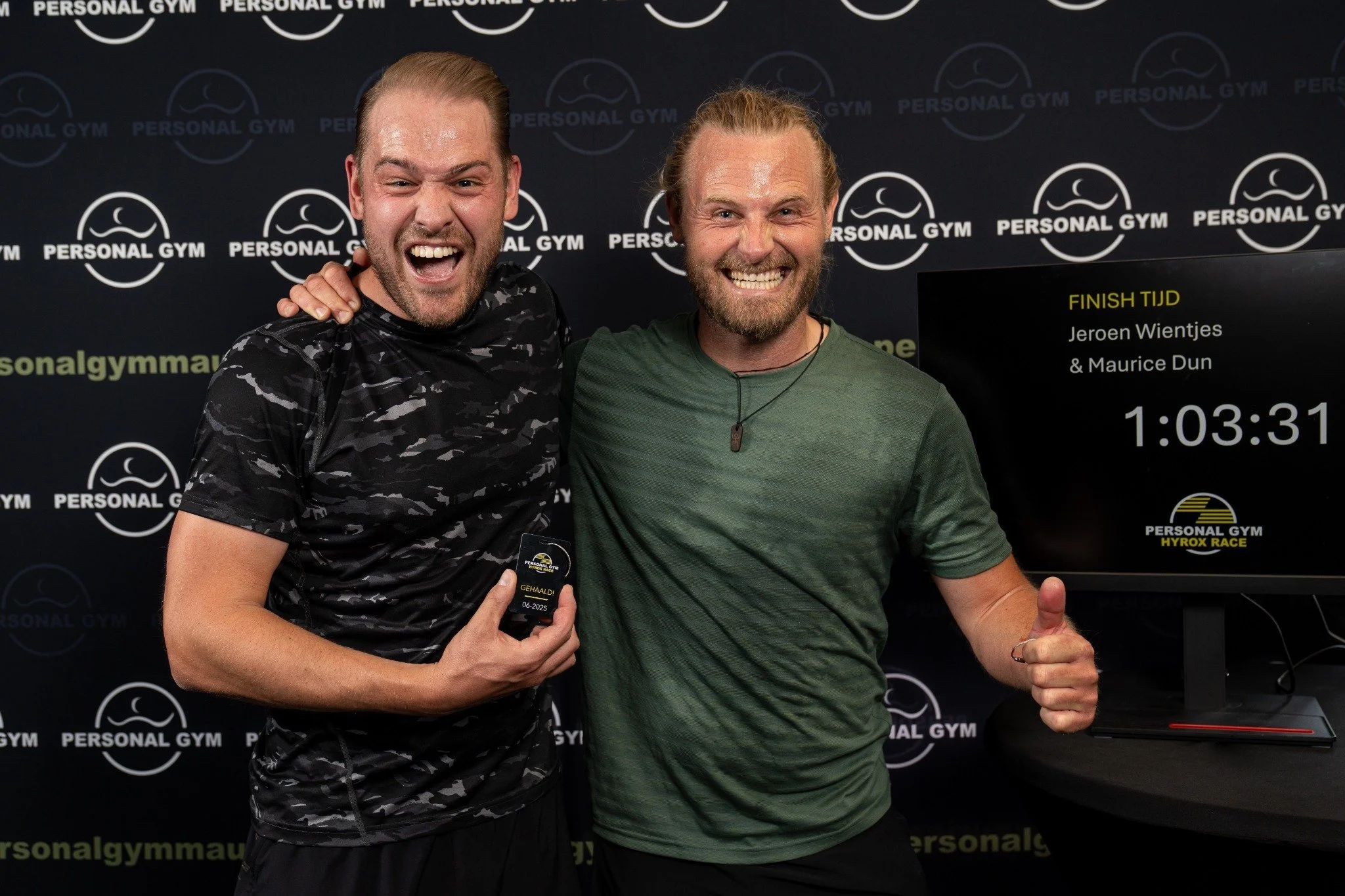Twee mannen vieren hun hardloopwedstrijd, één houdt een medaille vast, ze glimlachen en geven elkaar een high five. Achtergrond met 'Personal Gym' en een digitale timer die 1:03:31 toont.