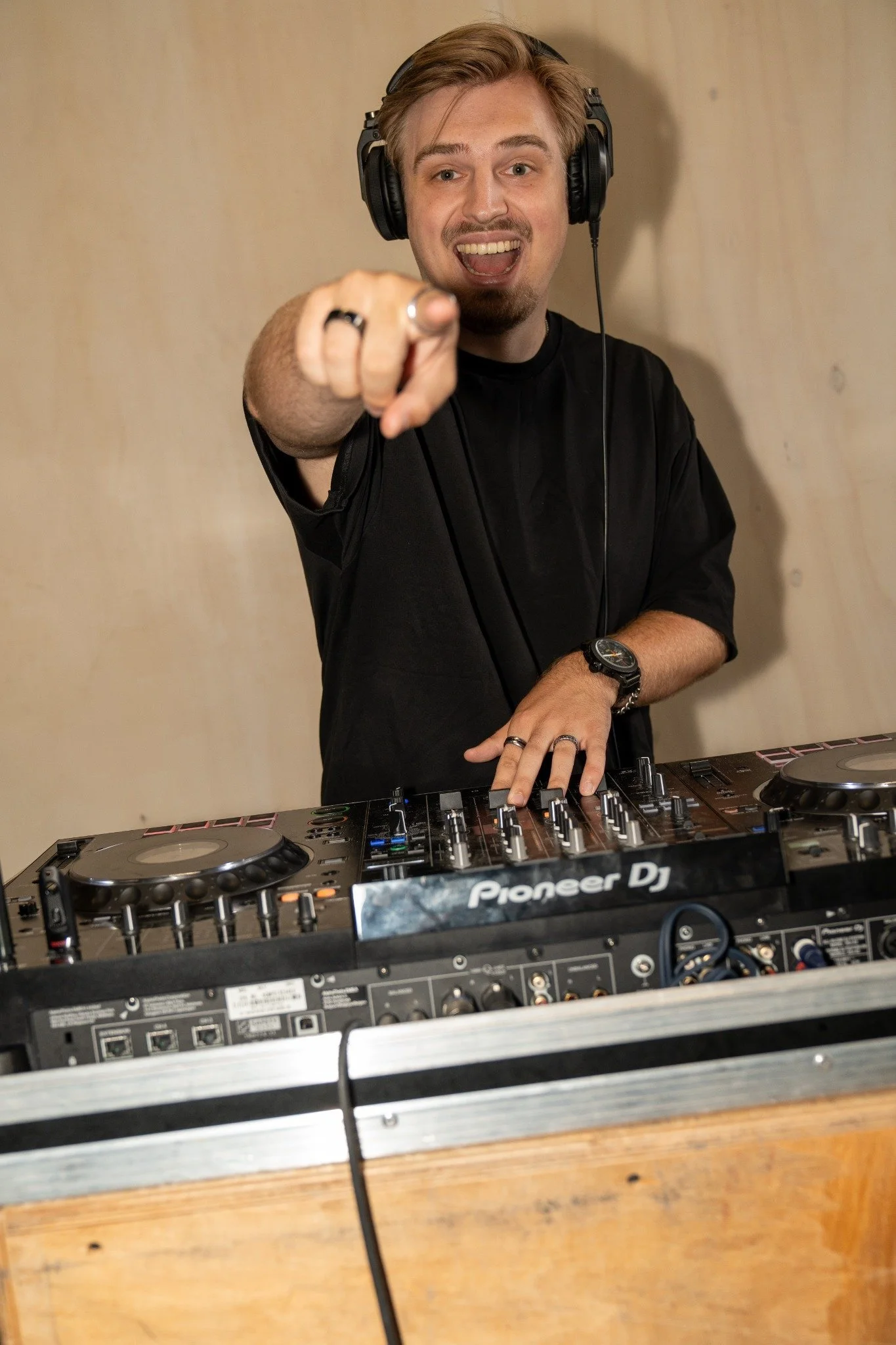 Man met koptelefoon die naar de camera wijst en achter een DJ-controller staat.