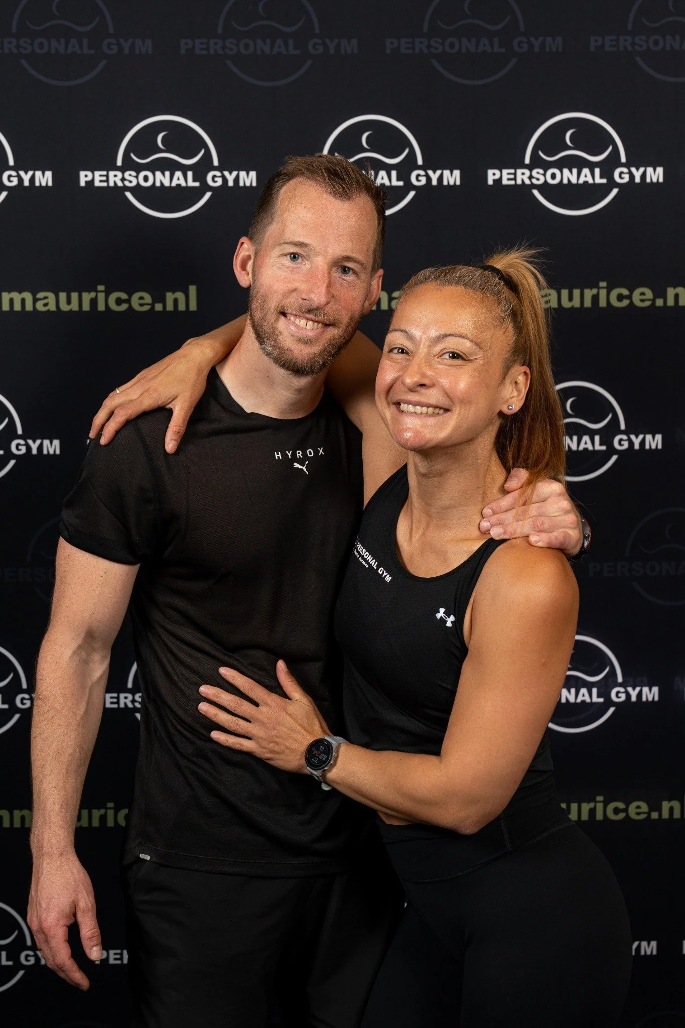 Twee mensen in sportkleding glimlachen en poseren samen, ter gelegenheid van een fitness of sportschool evenement.