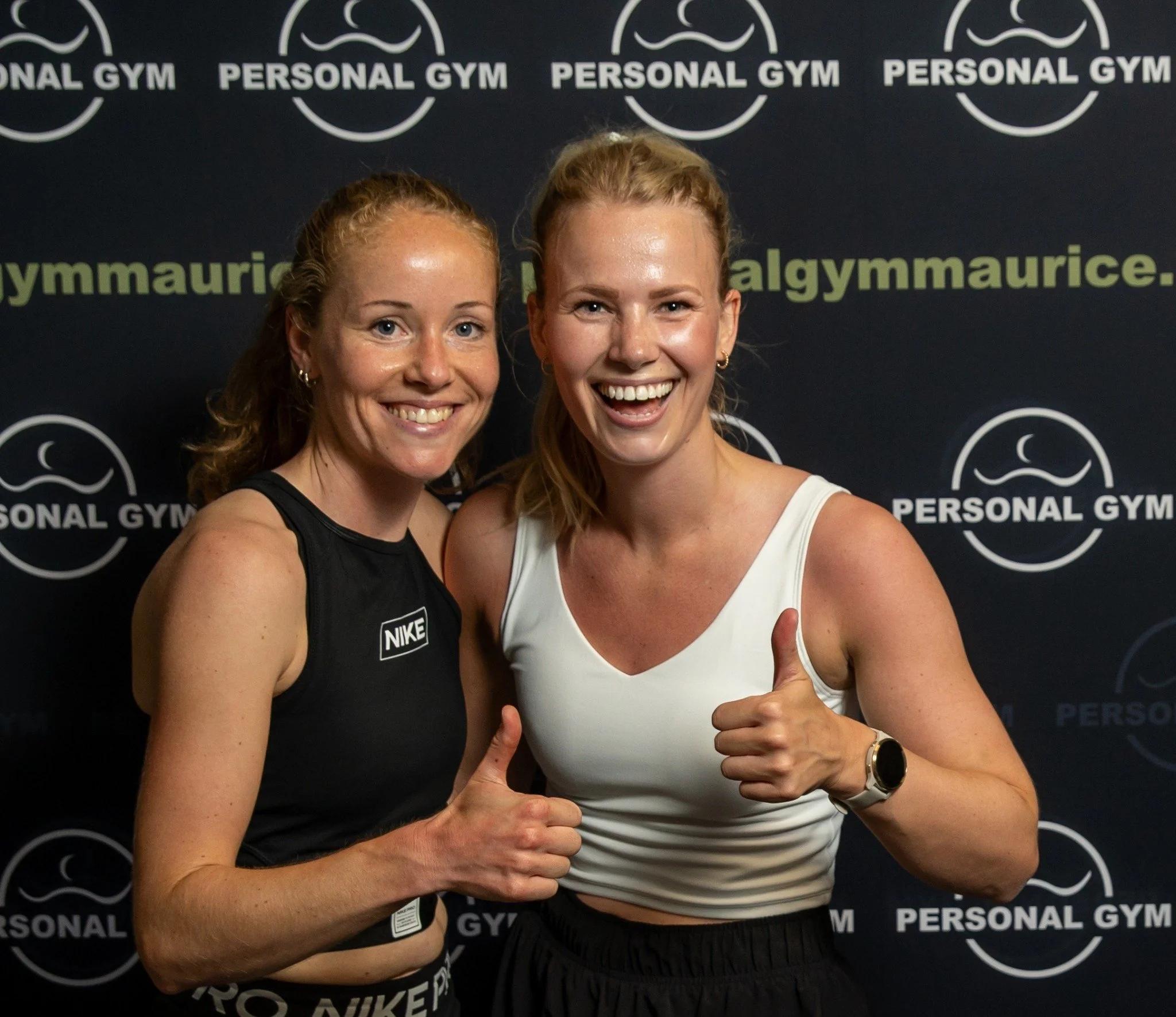 Twee vrouwen in sportkleding die glimlachen en een duim omhoog steken voor een zwarte achtergrond met het logo en tekst 'Personal Gym'.