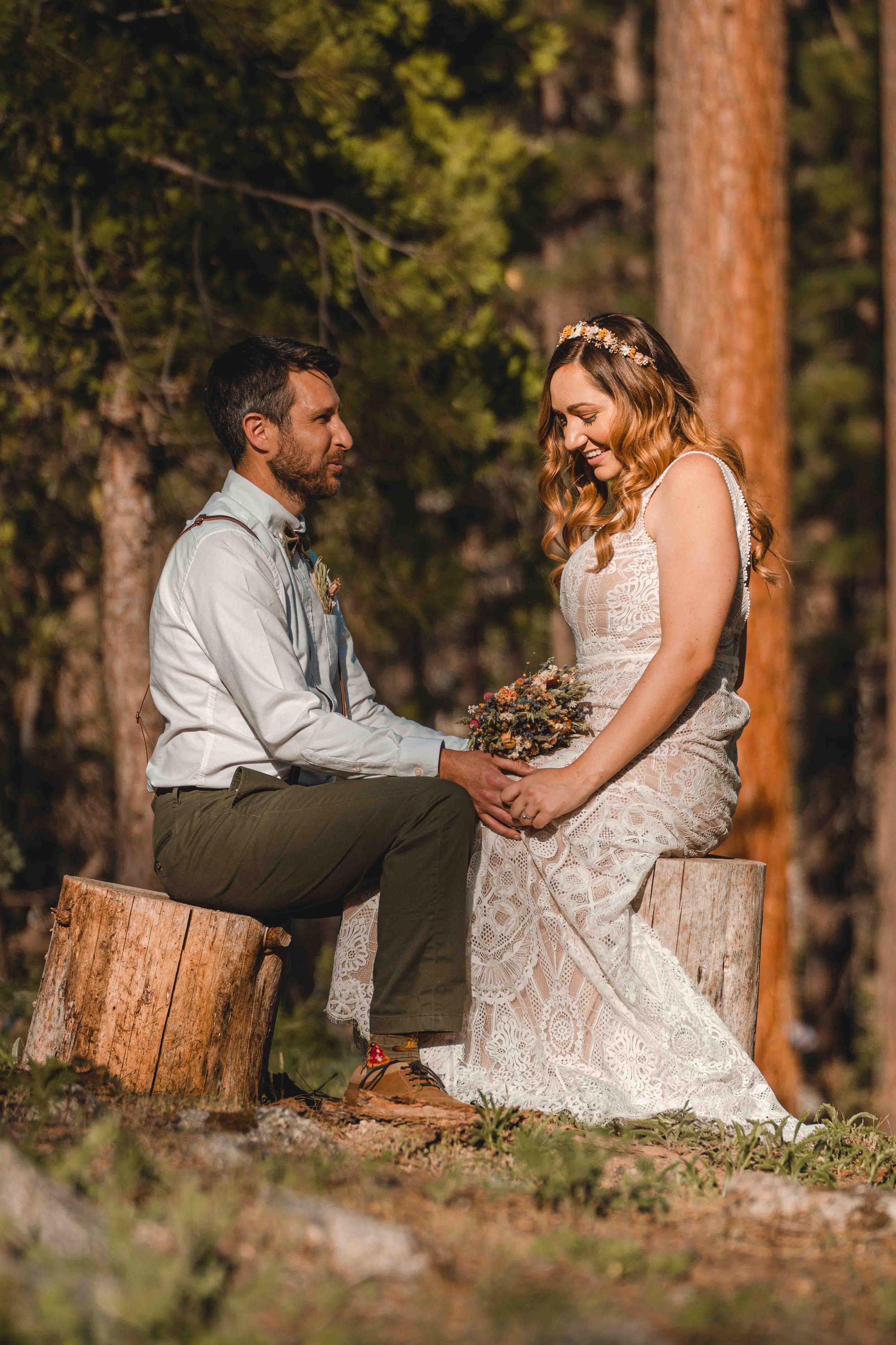 Bride and groom sitting on small logs facing eachother