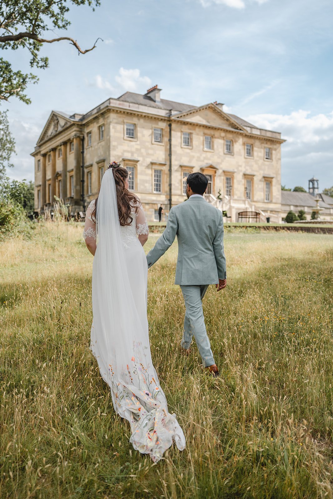 Dorothea and Peter walking away from camera through wedding venue gardens