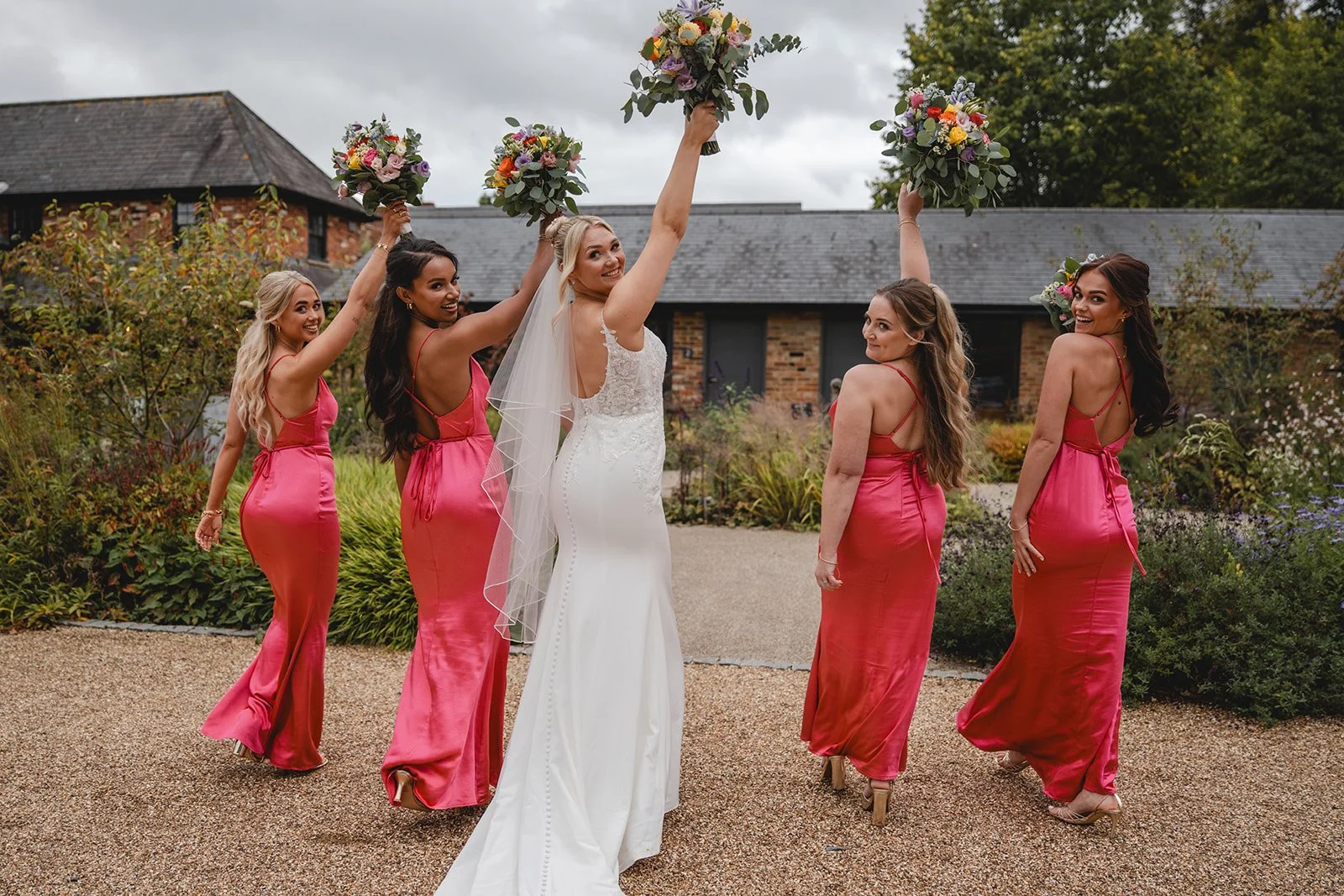 Kirsten and bridesmaids lifting bouquets outside the wedding venue