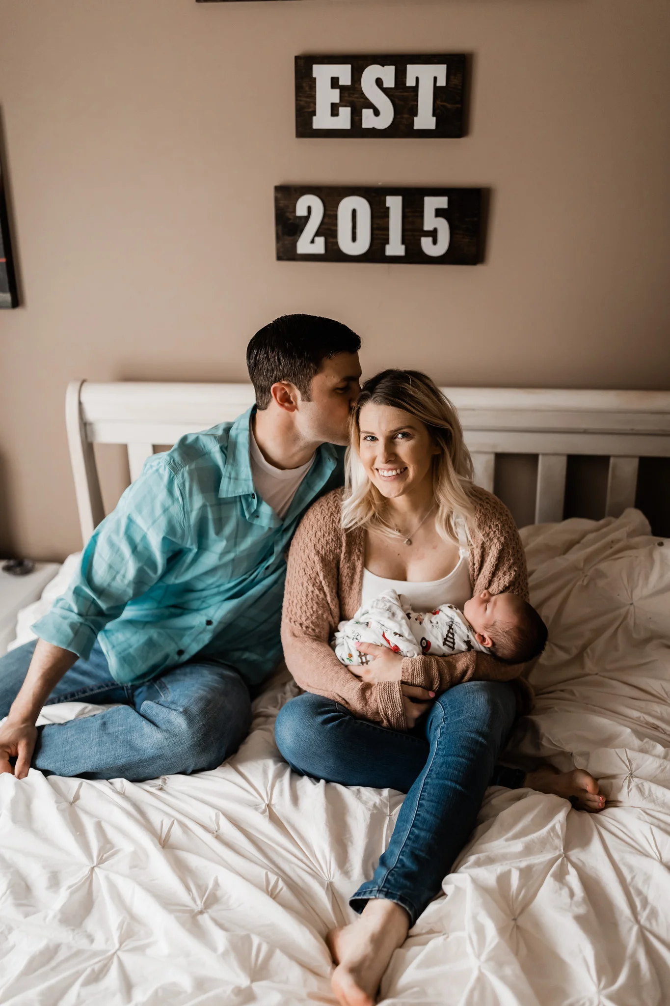 man kissing woman holding newborn