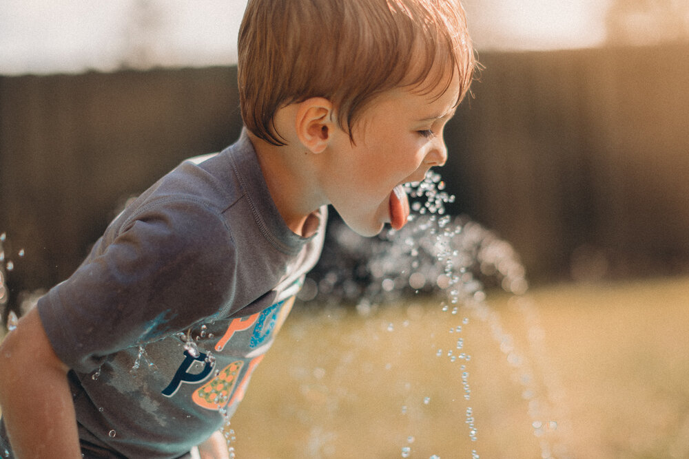 little boy drinking from sprinkler