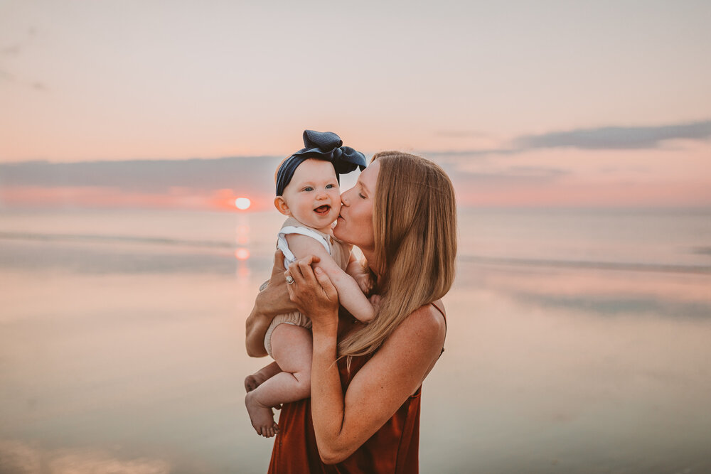 mom kissing baby on beach sunrise in savannah
