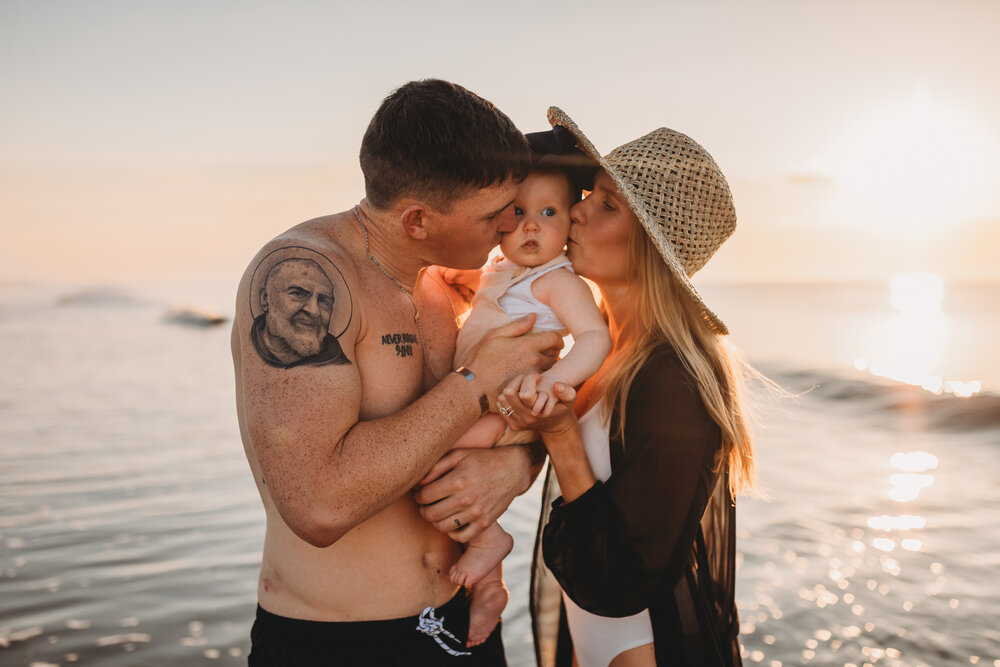 mom and dad kissing daughter on beach at sunrise jekyll island