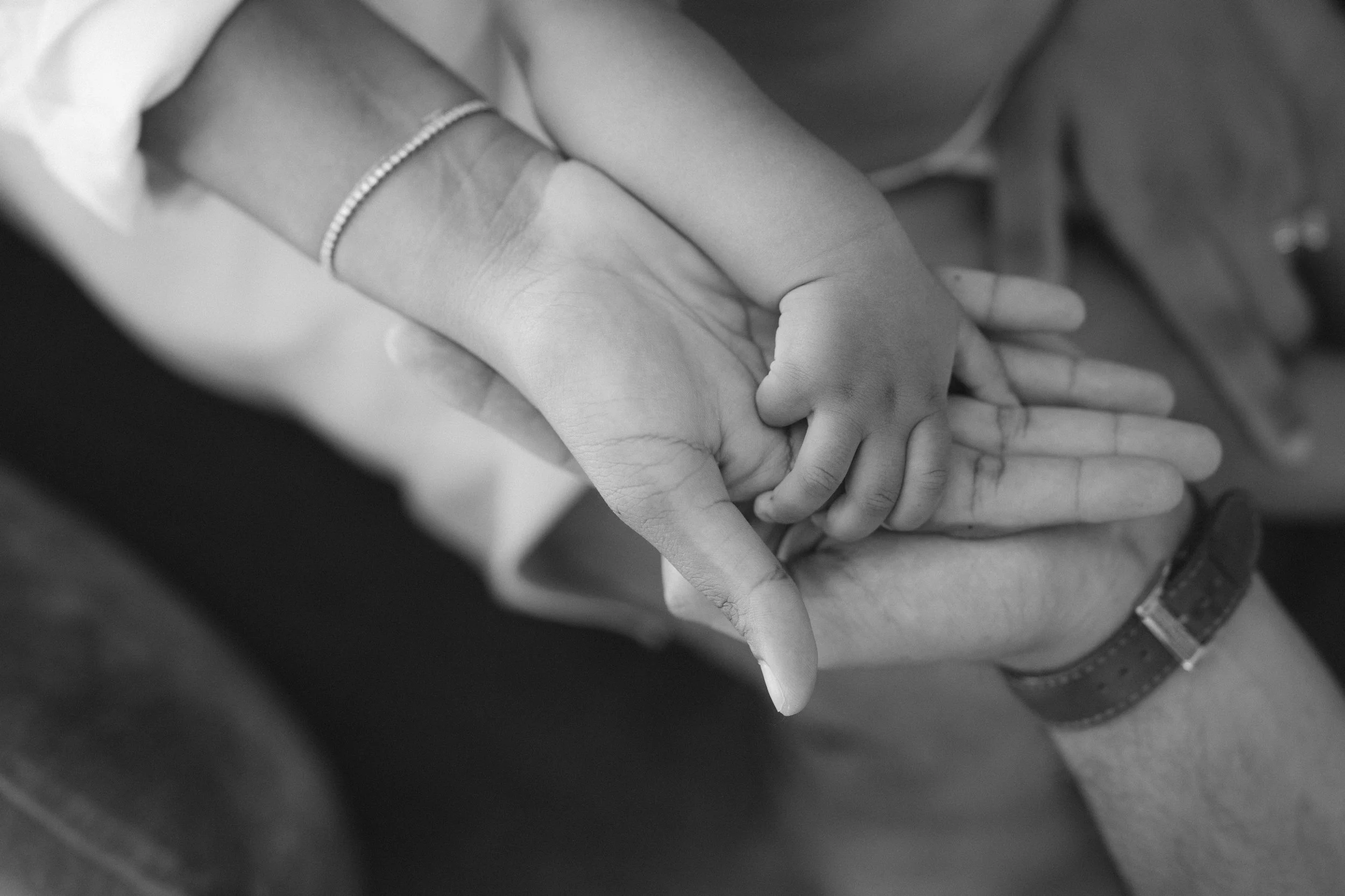 A family of three holding hands one on top of the other with the newborn baby hand on top
