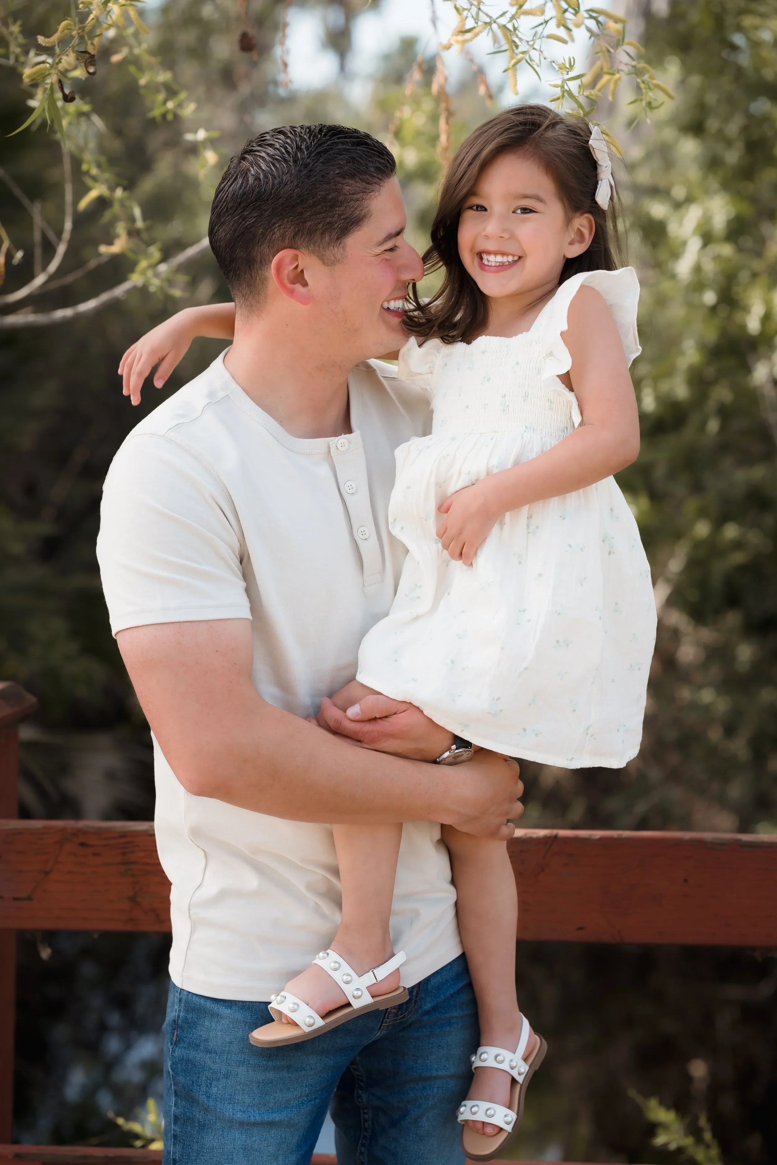 A father holding his young girl, both smiling and outdoors surrounded by trees at Eldorado park