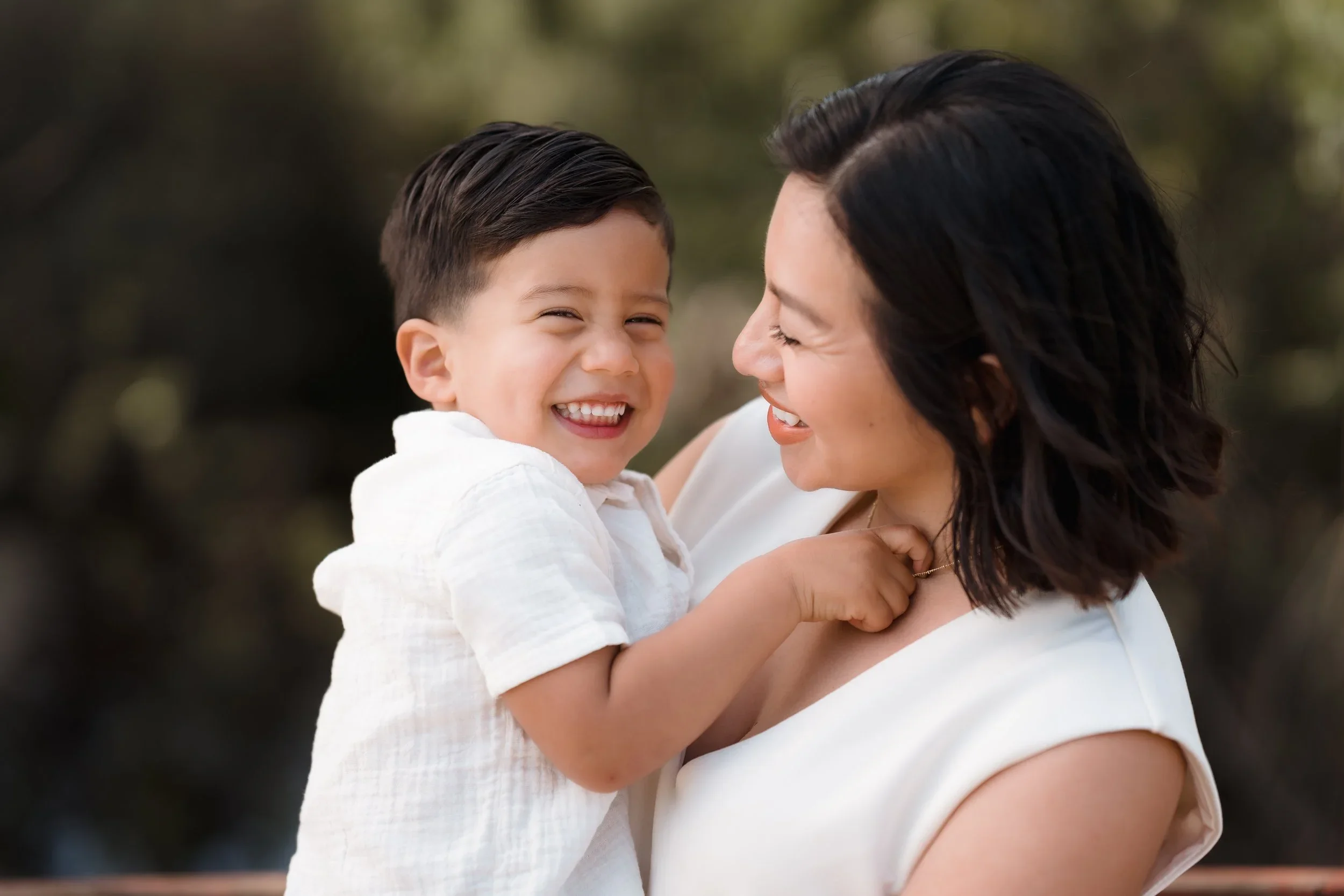 A mom smiling while holding her young boy who is also smiling, outdoors at Eldorado Park