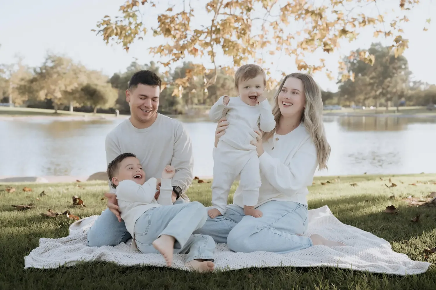 A family of four sitting on a blanket in Eldorado Park by a lake, smiling and playing together during autumn.