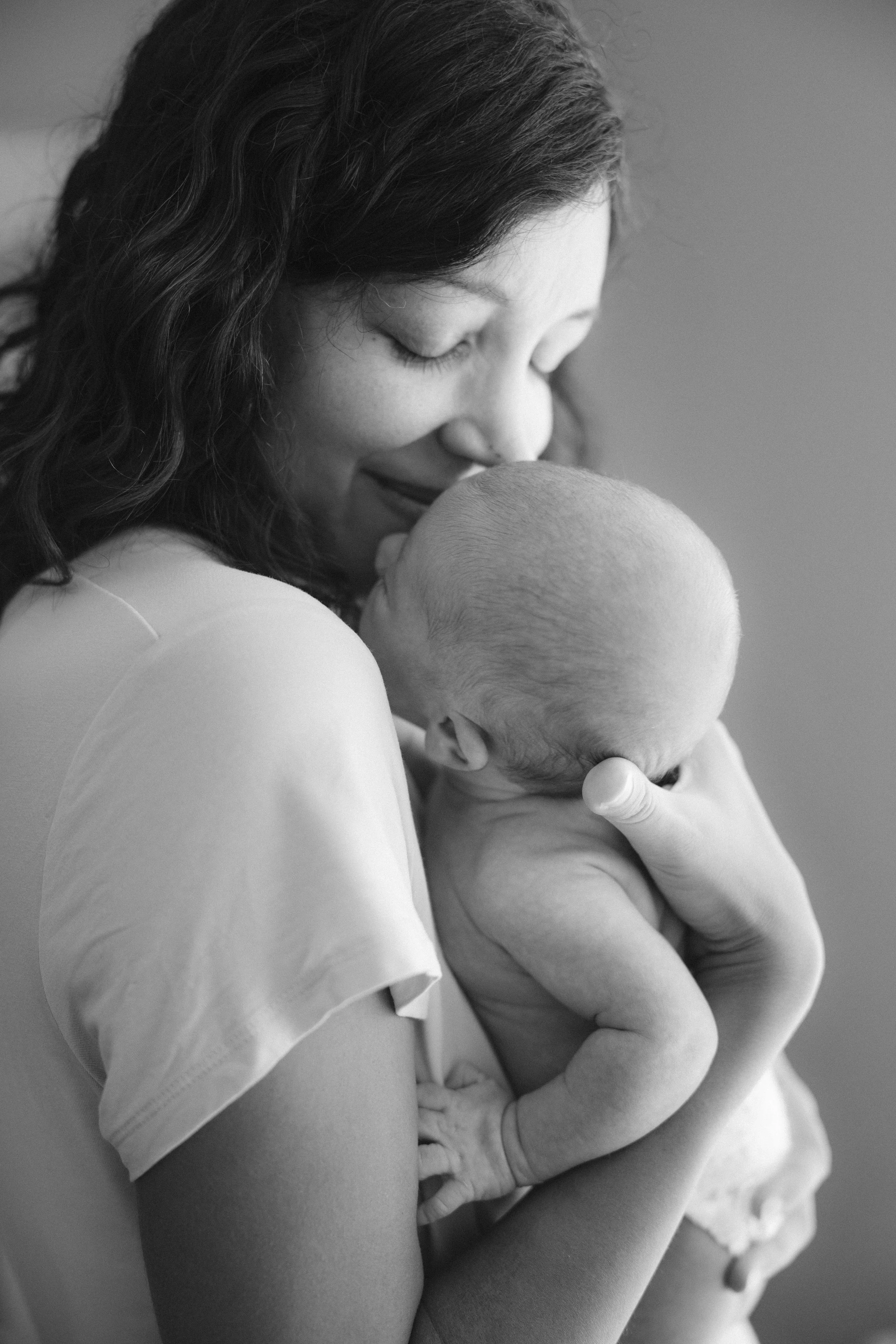 A woman with long, wavy hair holding a baby close to her chest, with her eyes closed and smiling softly, in black and white.