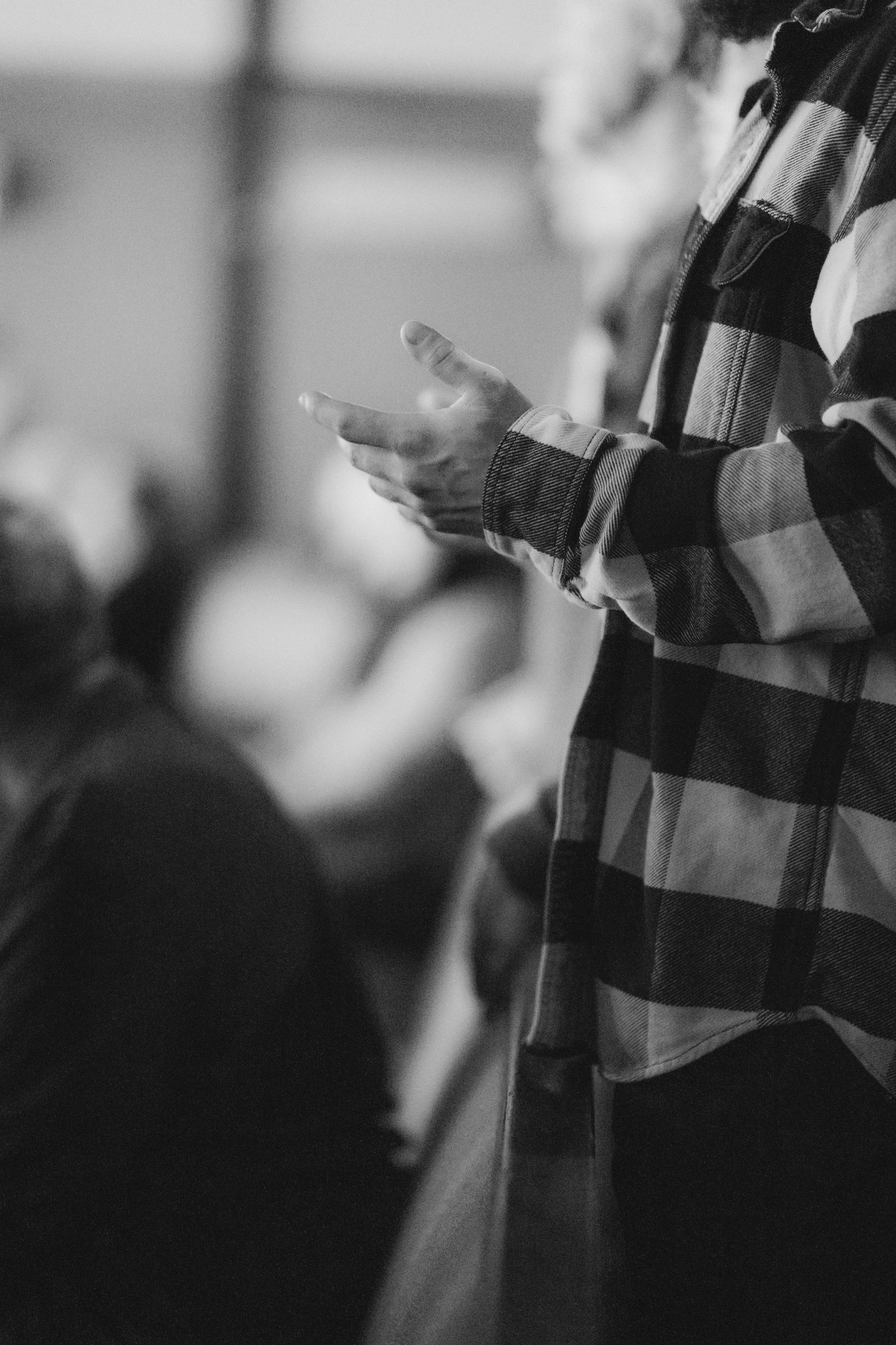 A person wearing a plaid shirt is looking at their phone with other people blurred in the background.