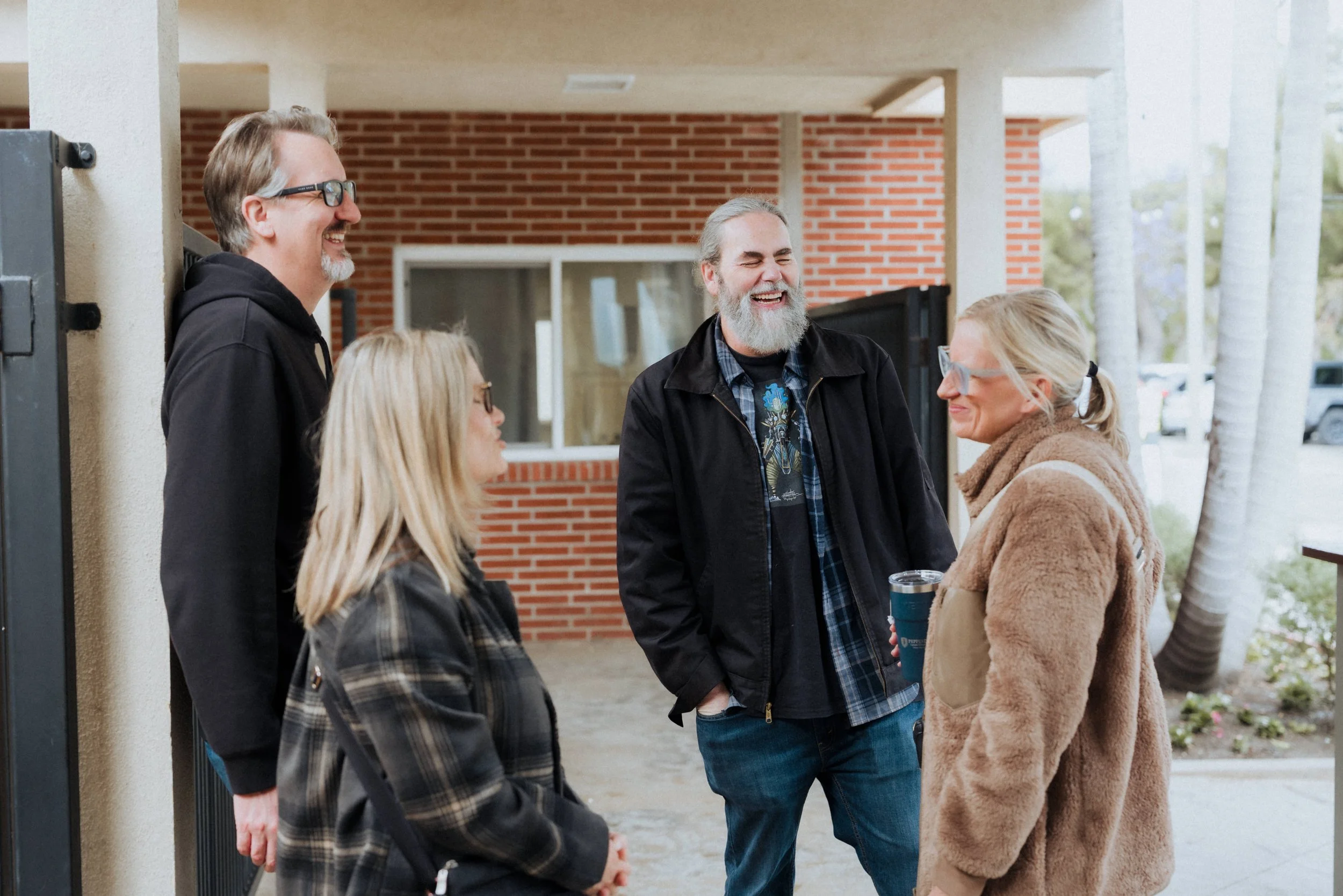 Four adults chatting outside a building, smiling and laughing, during daytime.
