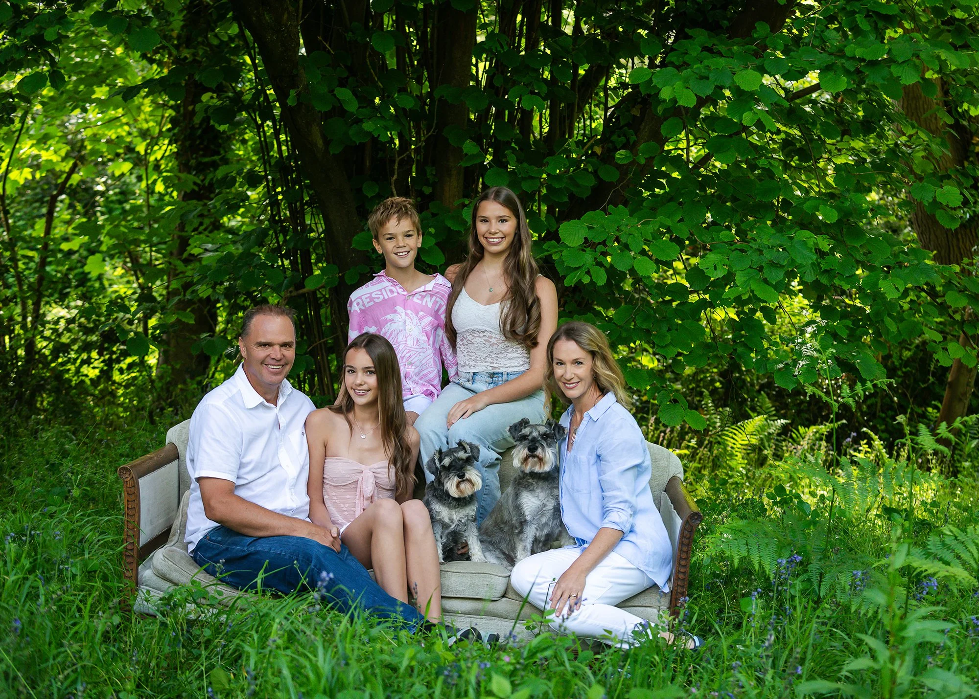 family on a sofa in a bluebell wood with two dogs