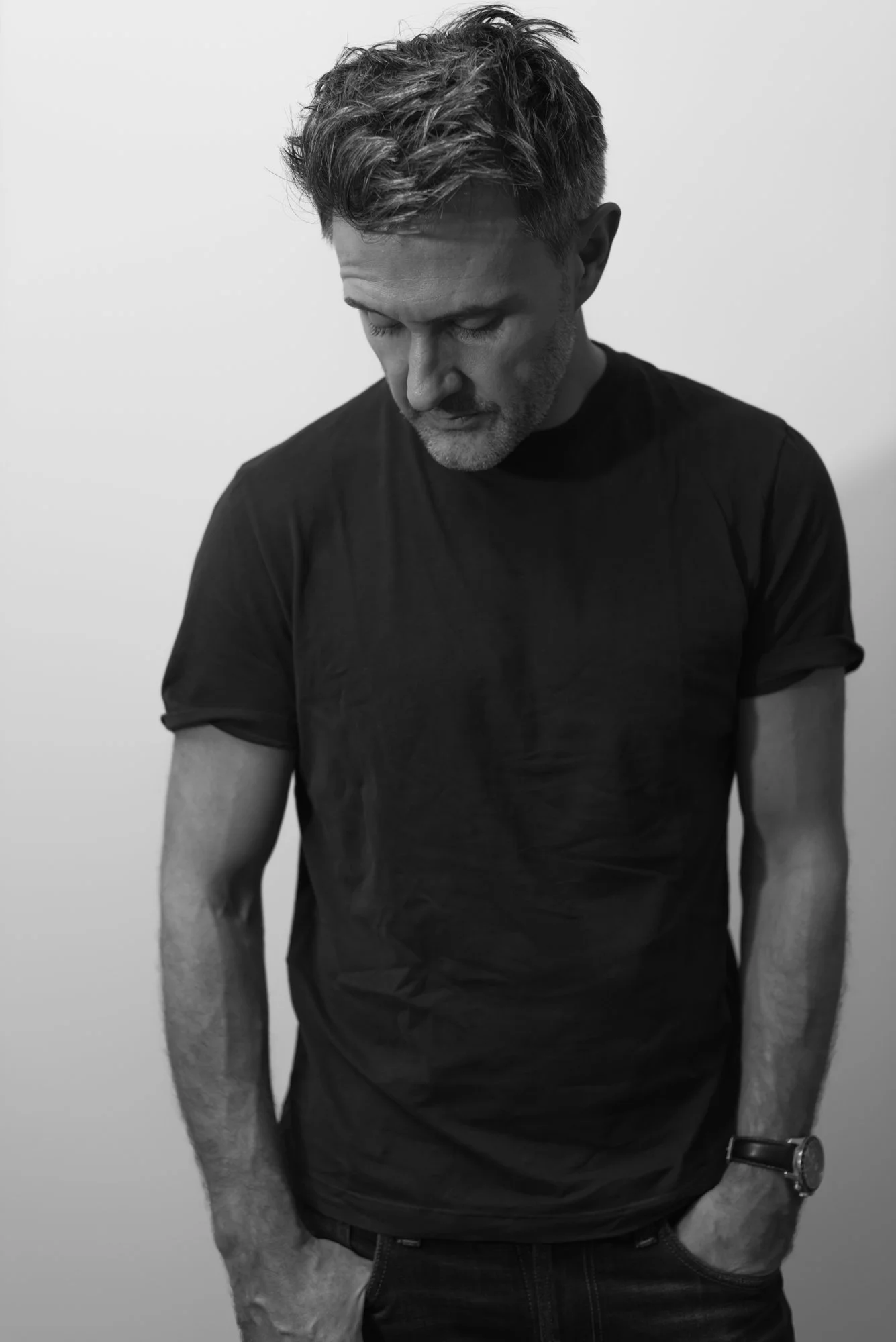 man in dark clothes with hands in pockets looking down