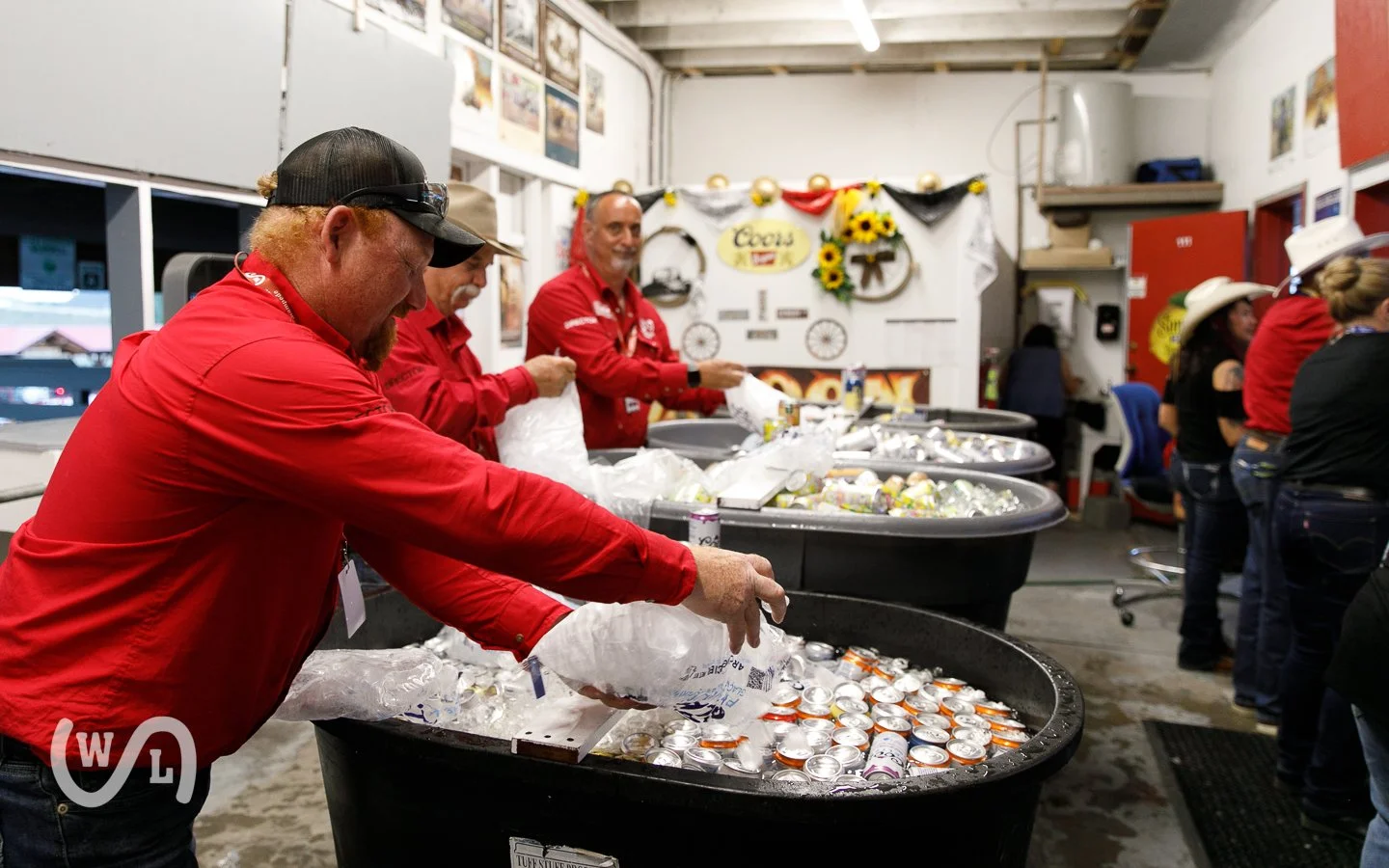 People in red shirts preparing and distributing cans of beer in large coolers at a community event.