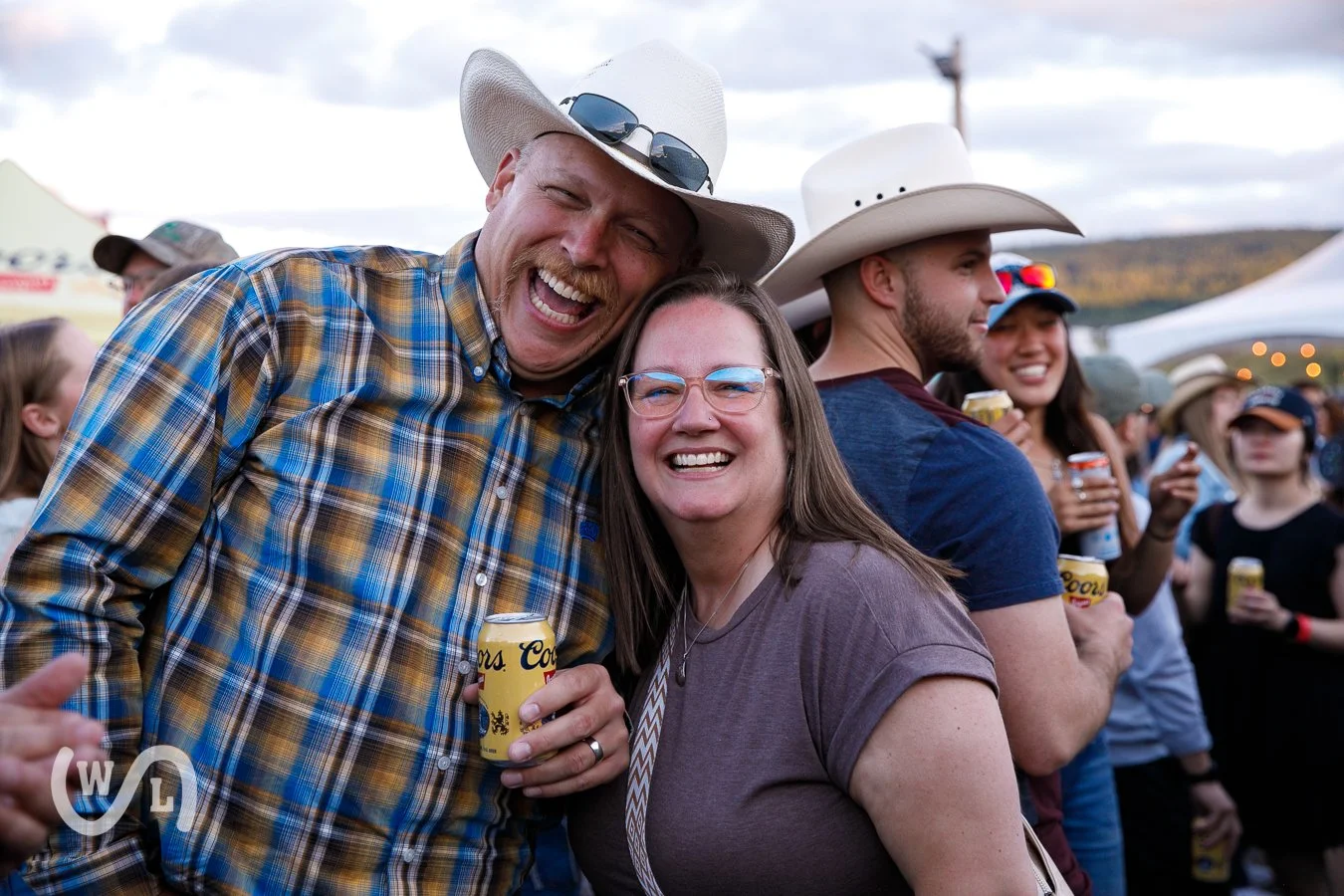 A group of people at an outdoor event, smiling and enjoying drinks, with some wearing cowboy hats and casual attire.