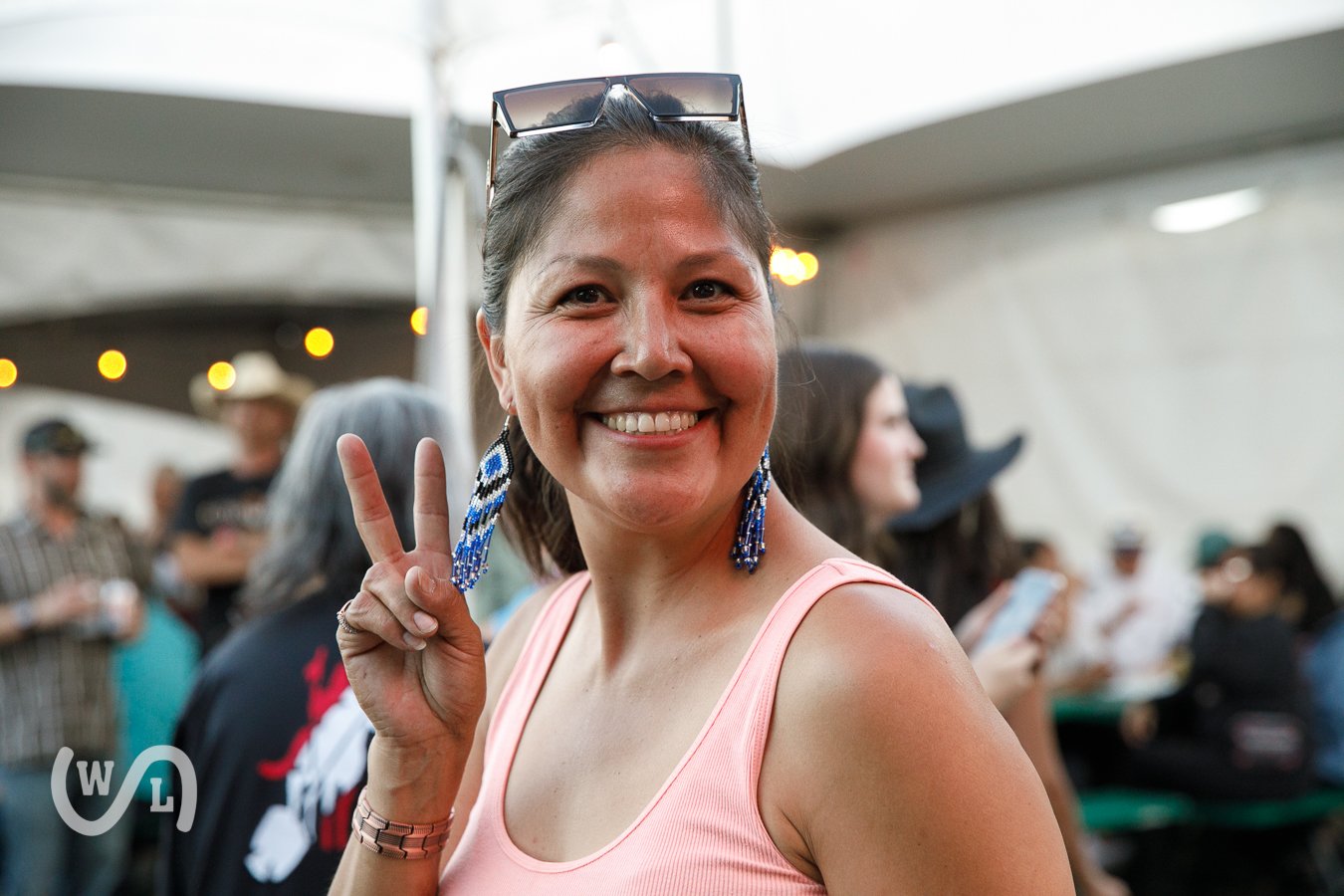 Smiling woman with earrings making a peace sign at an indoor event