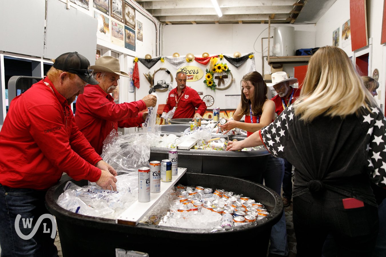 Group of people organizing and packing canned beverages in a room decorated with sunflower and farm-themed decor for a charity event.