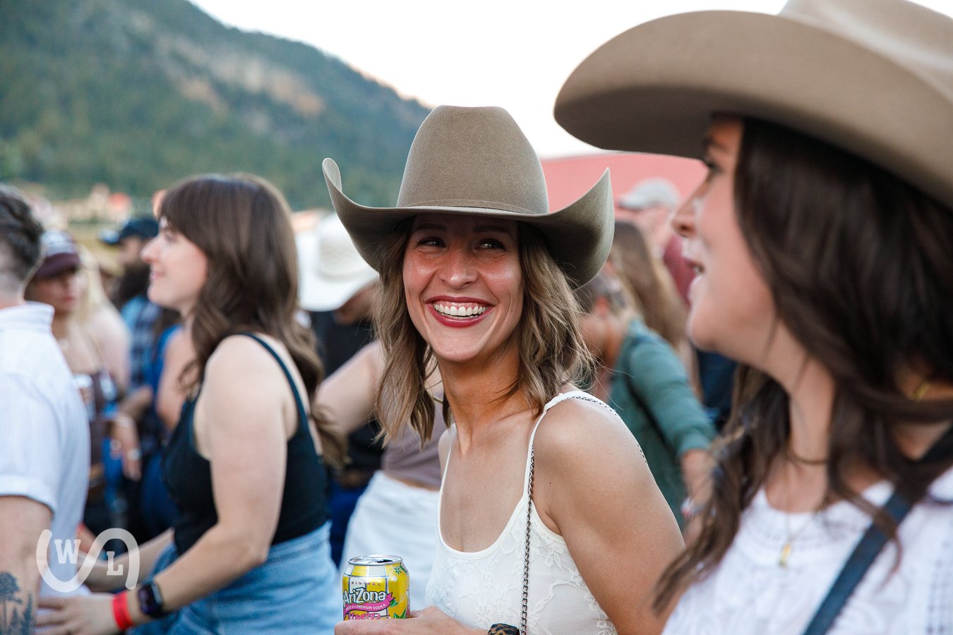 Group of people at an outdoor event, women wearing cowboy hats and smiling, with mountains in the background.