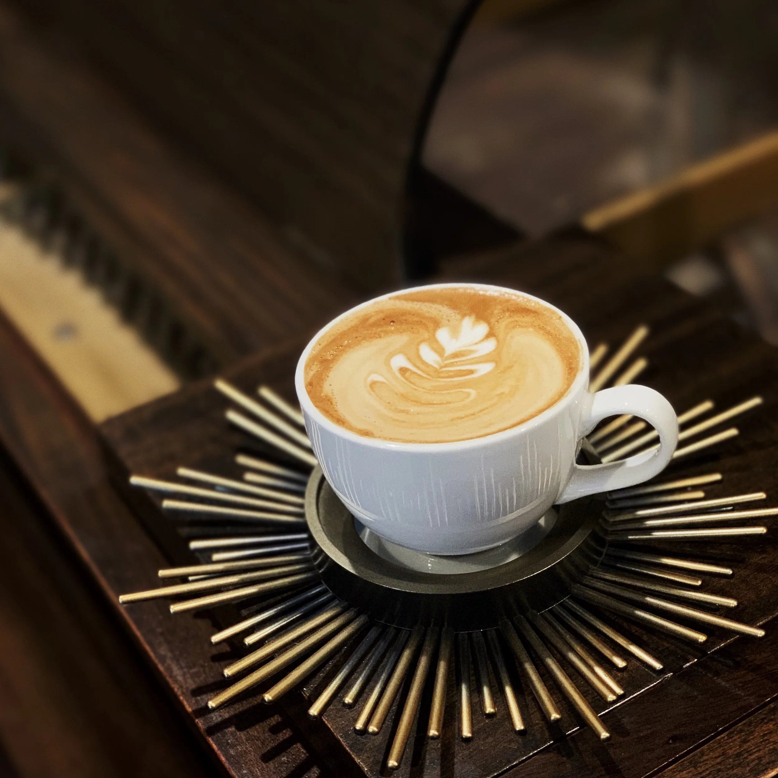 Rosetta Latte Art in a classic white cup in a gold cup holder on top of piano at Americano Coffee Lounge 434 Houston Street Suite 120 Nashville Tennessee 37203.