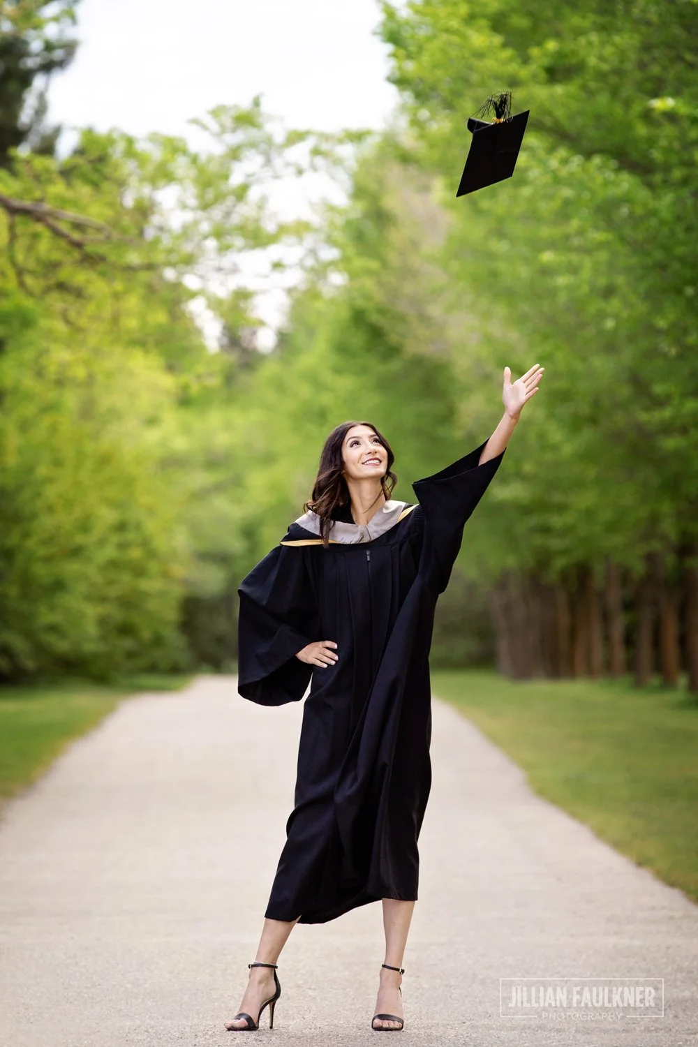 graduation photo of female university graduate on pathway tossing graduation hat a Baker Park in Calgary, Alberta.