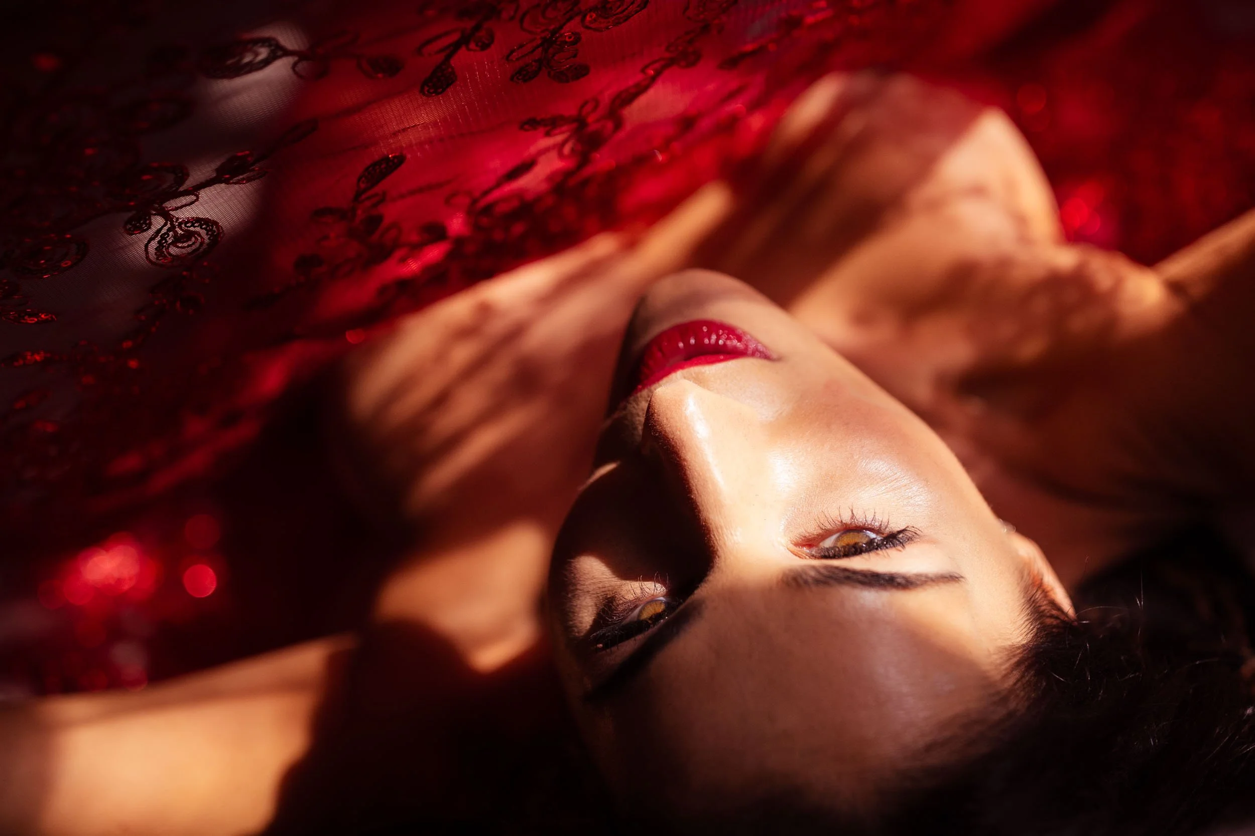 woman lying on back with red lace fabric above her