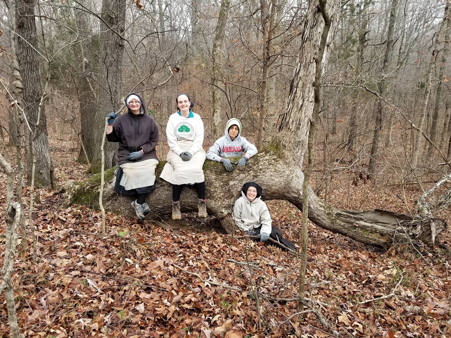  Sr. Miriam Esther, Postulant Abbey, Sr. Mary Andrea, and Sr. Frances Marie pose for a photo on the famous “dinosaur tree” in our woods 