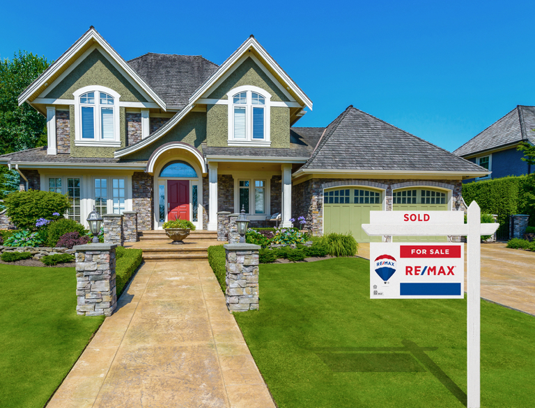 Two-story suburban house with stone accents, green lawn, and 'Sold' Re/Max sign.