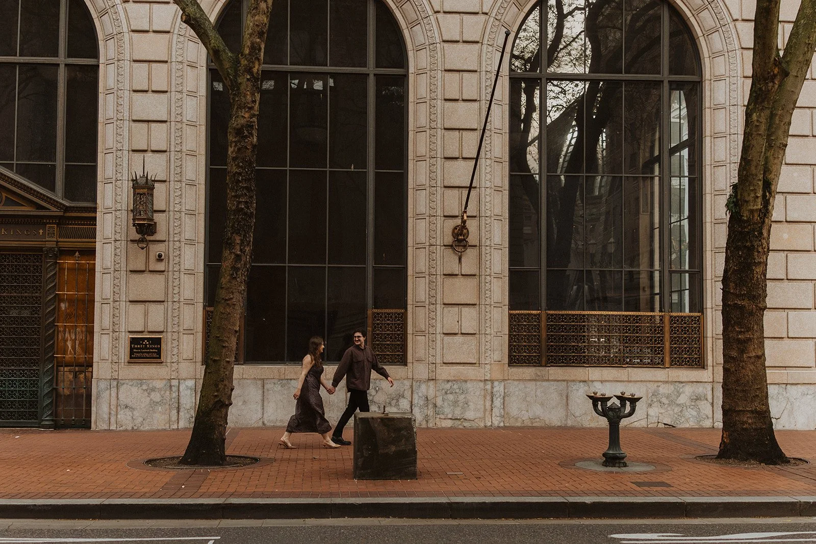 Couple walking hand in hand along a downtown Portland street with historic architecture during an engagement session
