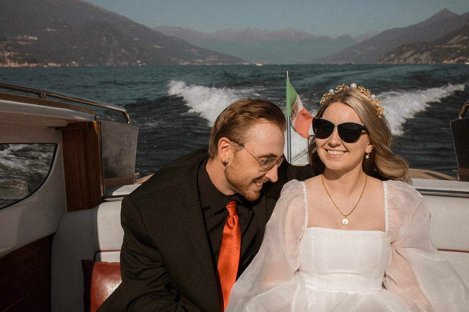 Bride and groom smiling together aboard a classic Lake Como boat during their intimate Italy elopement with mountain views behind them.