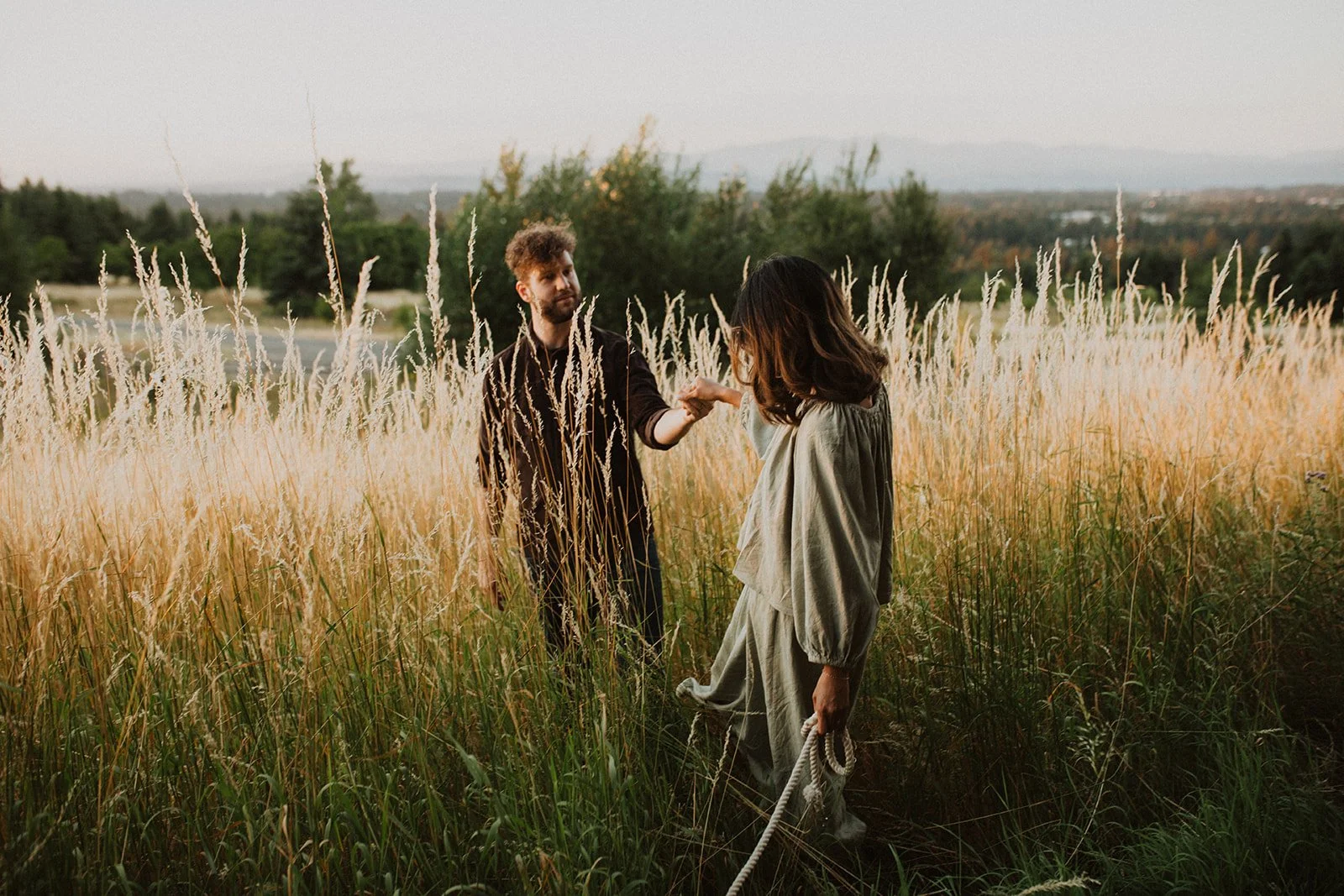 Couple holding hands and walking through tall grass at golden hour during an Oregon engagement session