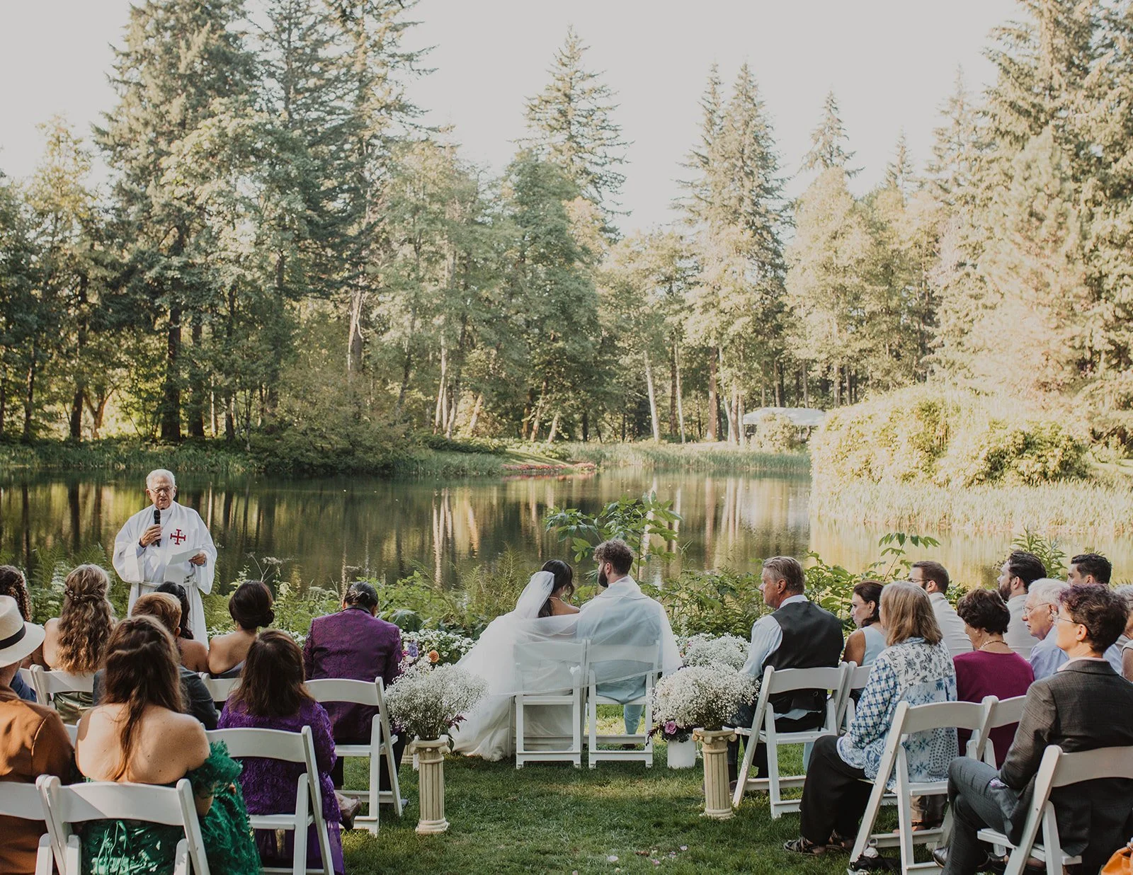 Officiant speaking at the water's edge while guests watch from the lawn