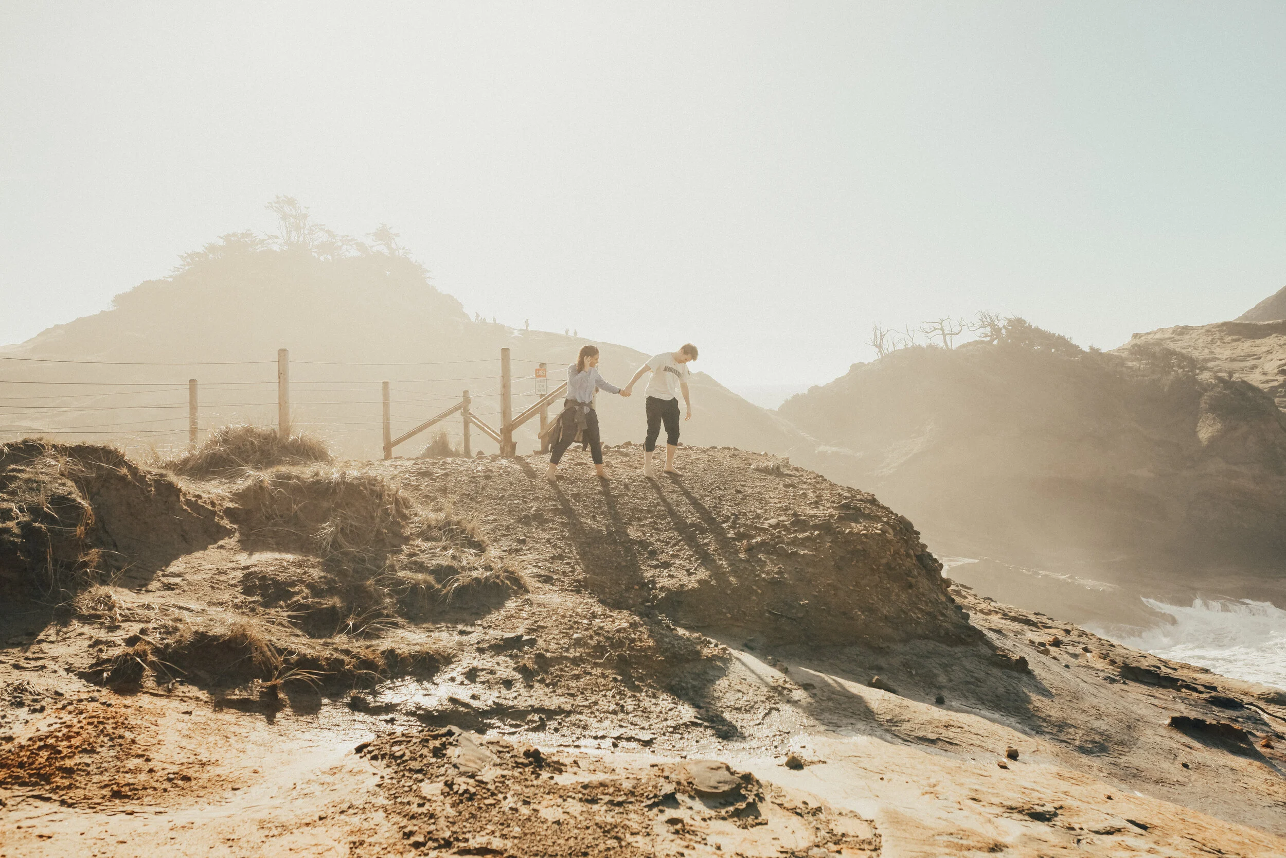 Couple running hand in hand along a misty coastal cliffside with dramatic scenery, captured by a wedding photographer in Portland Oregon.